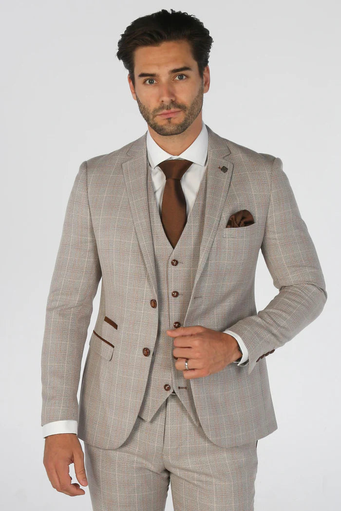 Close-up of a man wearing a beige check three-piece suit with brown tie and pocket square, showcasing modern tailored fit.