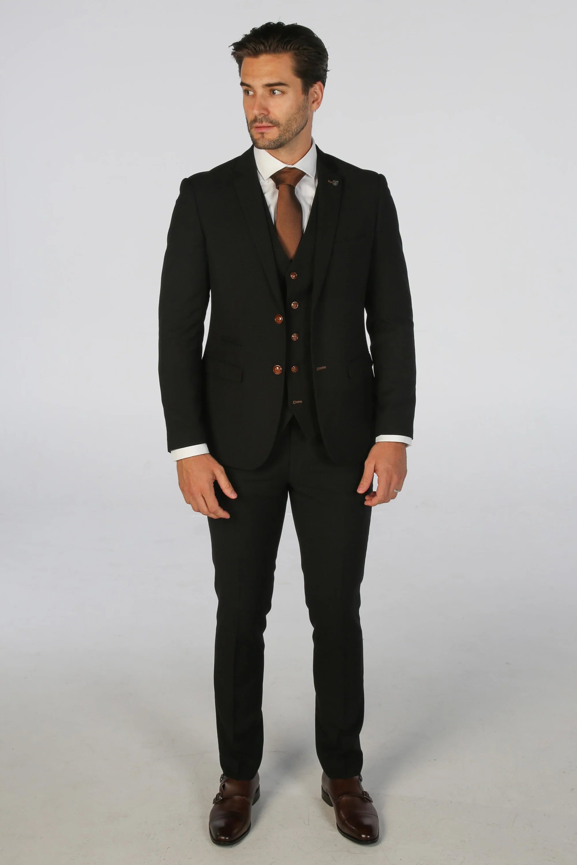 Full-body view of man in black textured suit, styled with a brown tie and dark shoes, standing against a light background.