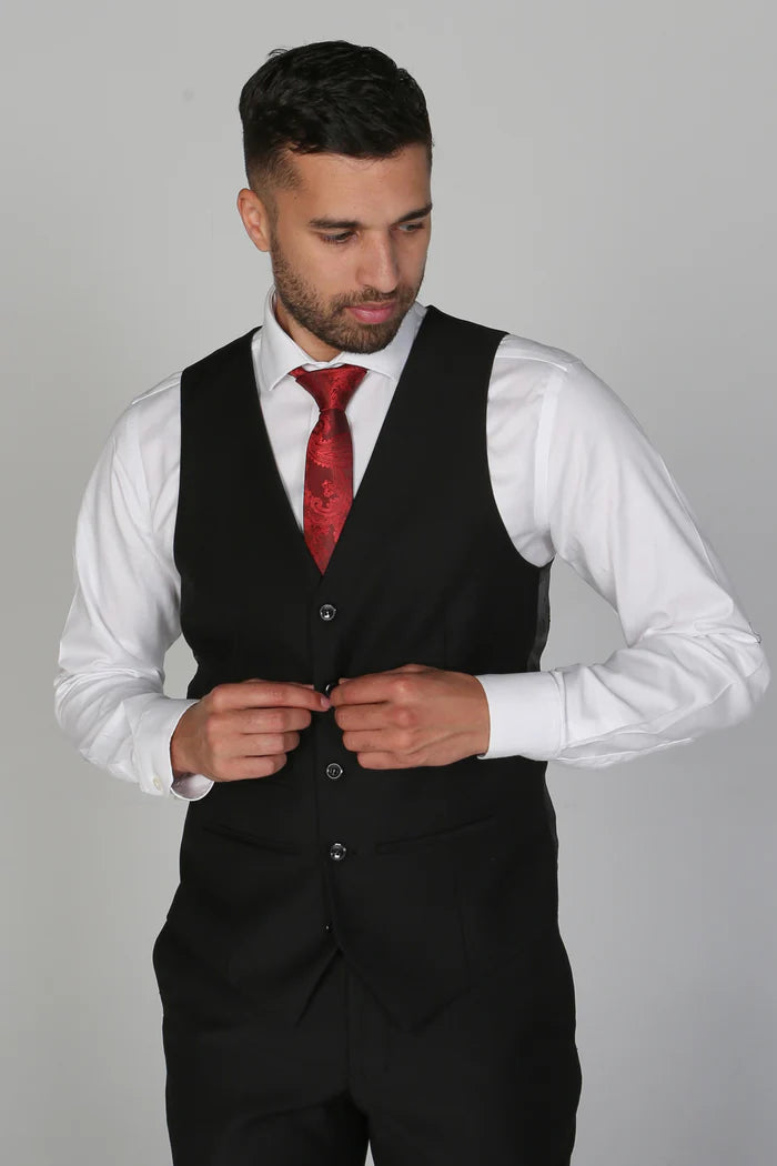 Model in a white shirt and red tie adjusting the front of a black waistcoat with classic button-up design.
