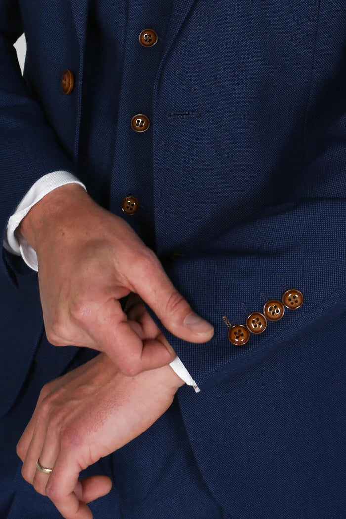 Close-up of the blazer cuff showing brown buttons and tailored detailing as a hand adjusts the sleeve.