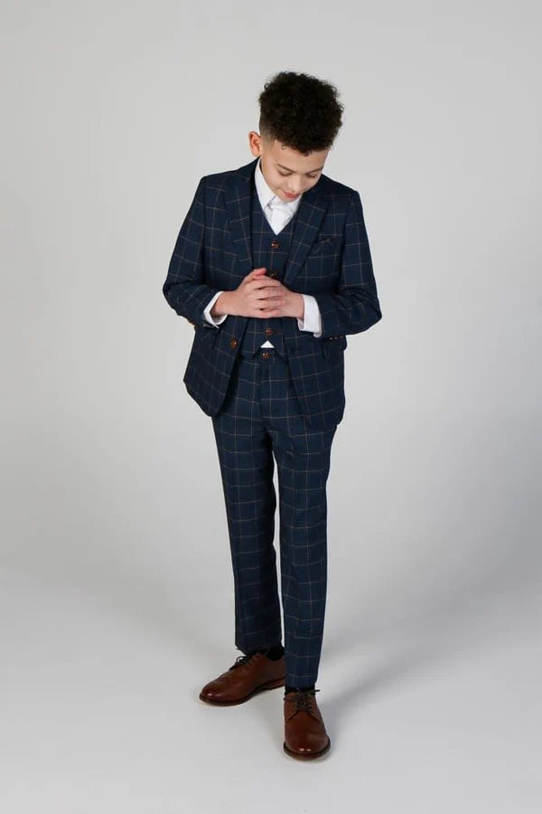 Boy in navy three-piece check suit looking down with clasped hands, demonstrating formal posture for special occasions.