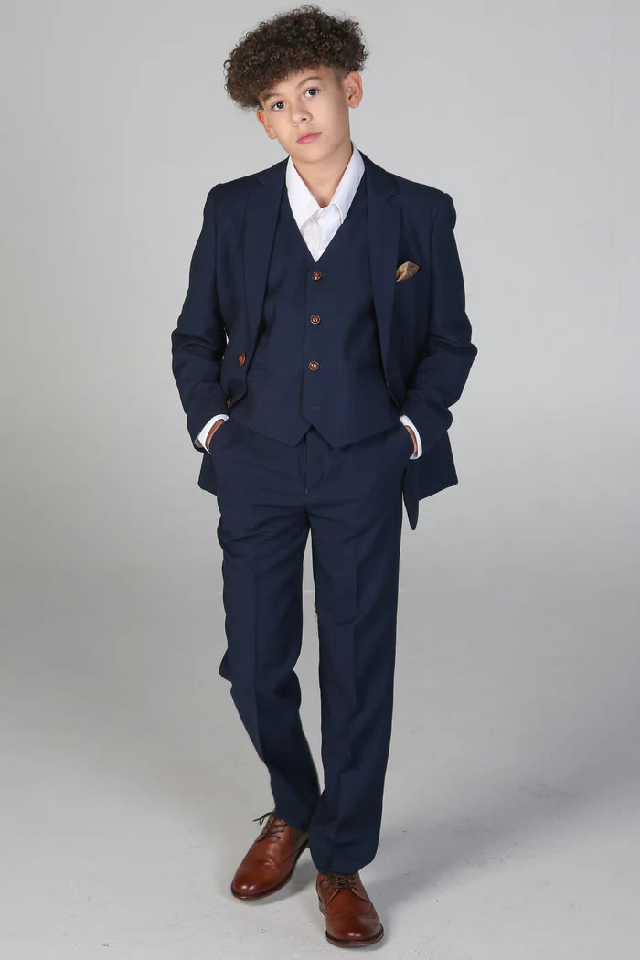 Full body view of boy in navy three-piece suit with tailored fit, white shirt, and brown dress shoes.