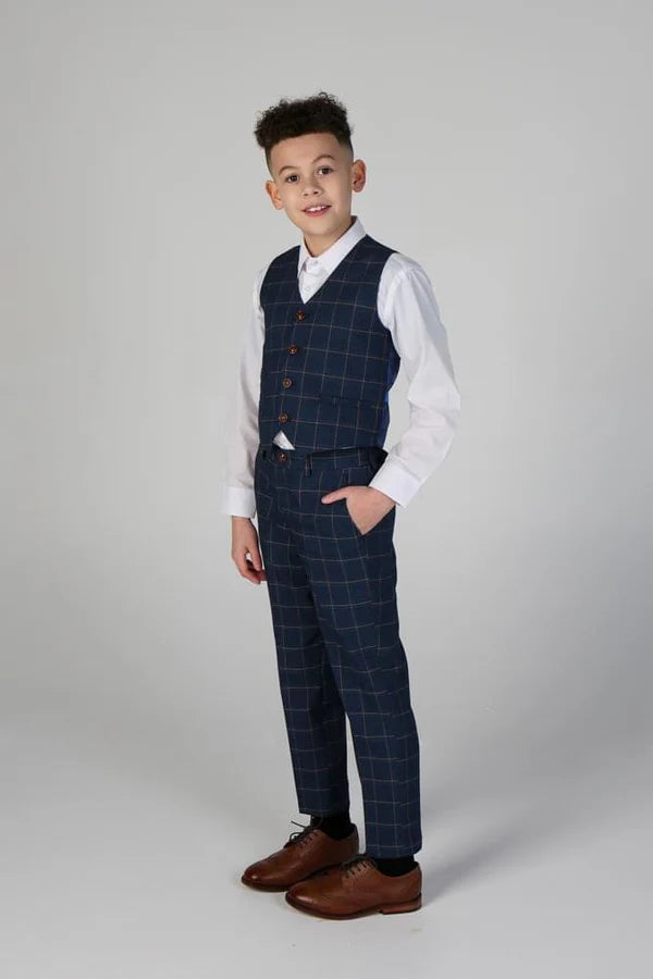 Side profile of boy wearing navy check waistcoat with matching trousers, white shirt and brown shoes, hand in pocket.
