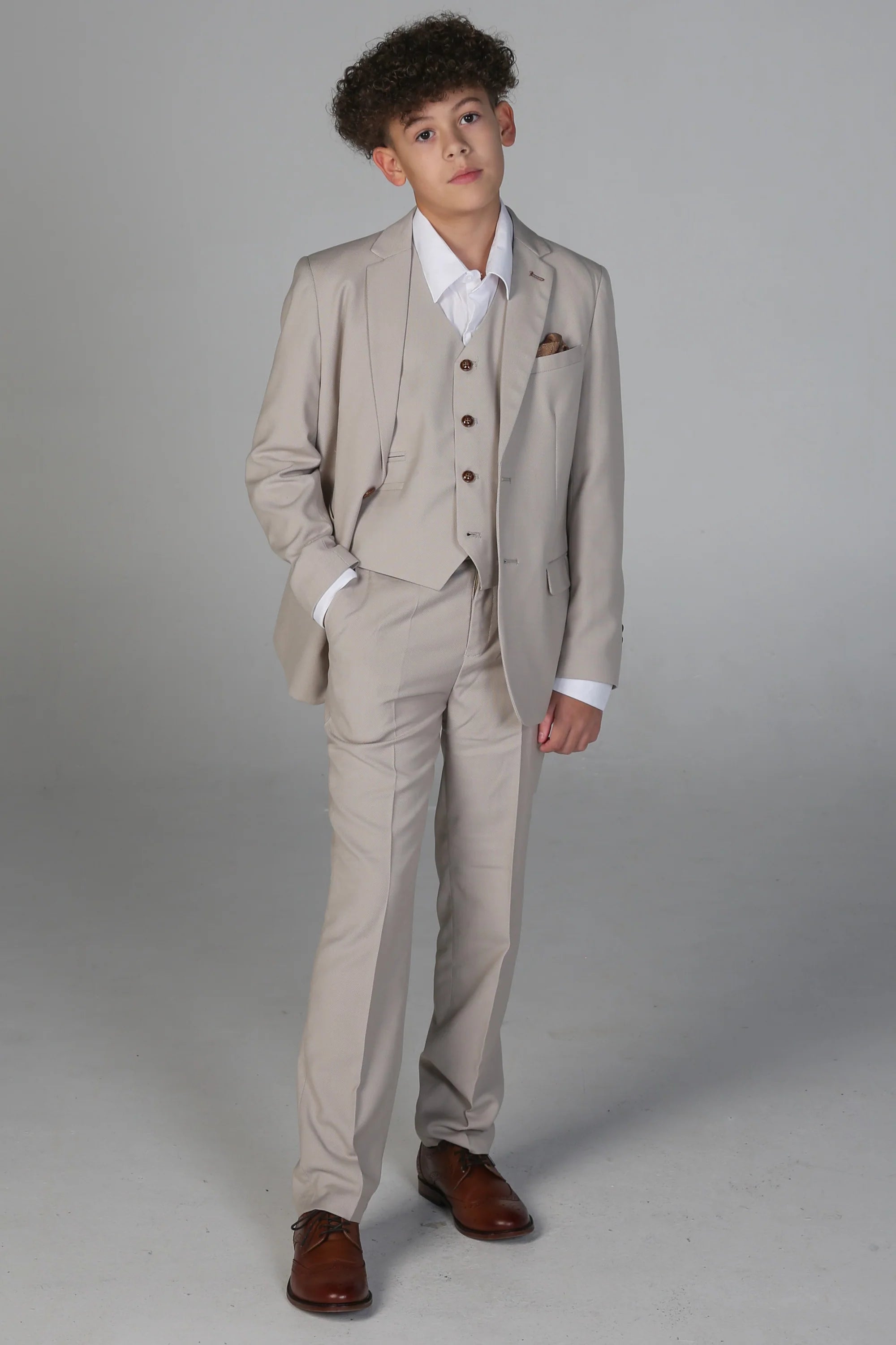 Full body view of boy in formal stone suit with tailored fit, white shirt, and brown dress shoes.