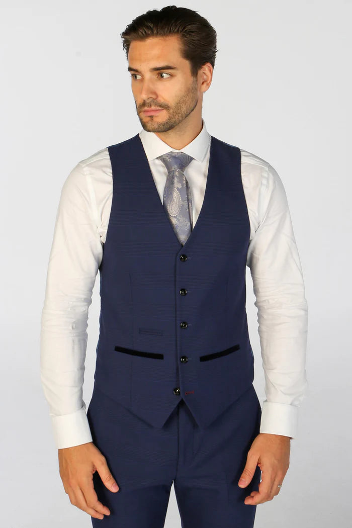 A man in a white shirt and navy blue check waistcoat with black trimmed pockets, looking to the side.