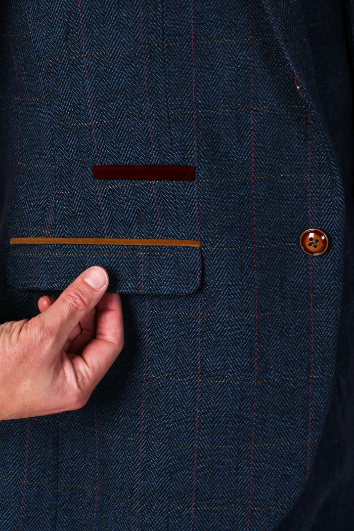 Close-up of navy tweed blazer pocket with contrast trim and visible stitching on the herringbone pattern fabric.