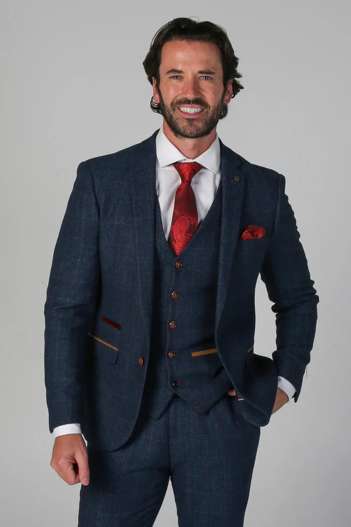 Man wearing a navy tweed check three-piece suit with red tie and pocket square, smiling in a front close-up.