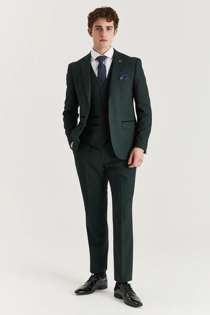 Full-body view of a man styled in an olive check three-piece suit, white shirt, and navy tie and pocket square