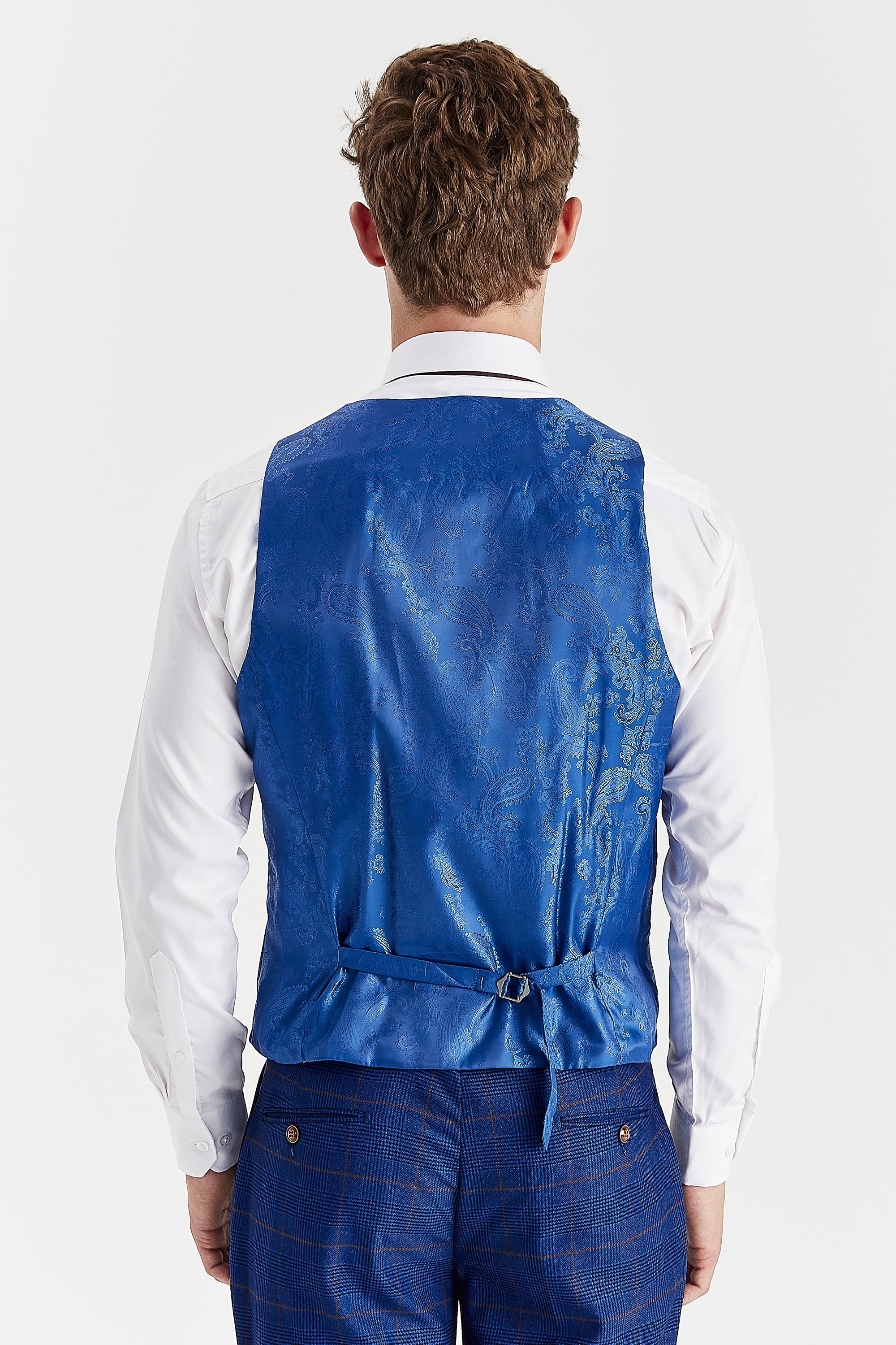 Rear view of the navy waistcoat with a blue paisley back panel and adjustable strap, worn with a white shirt and matching trousers.