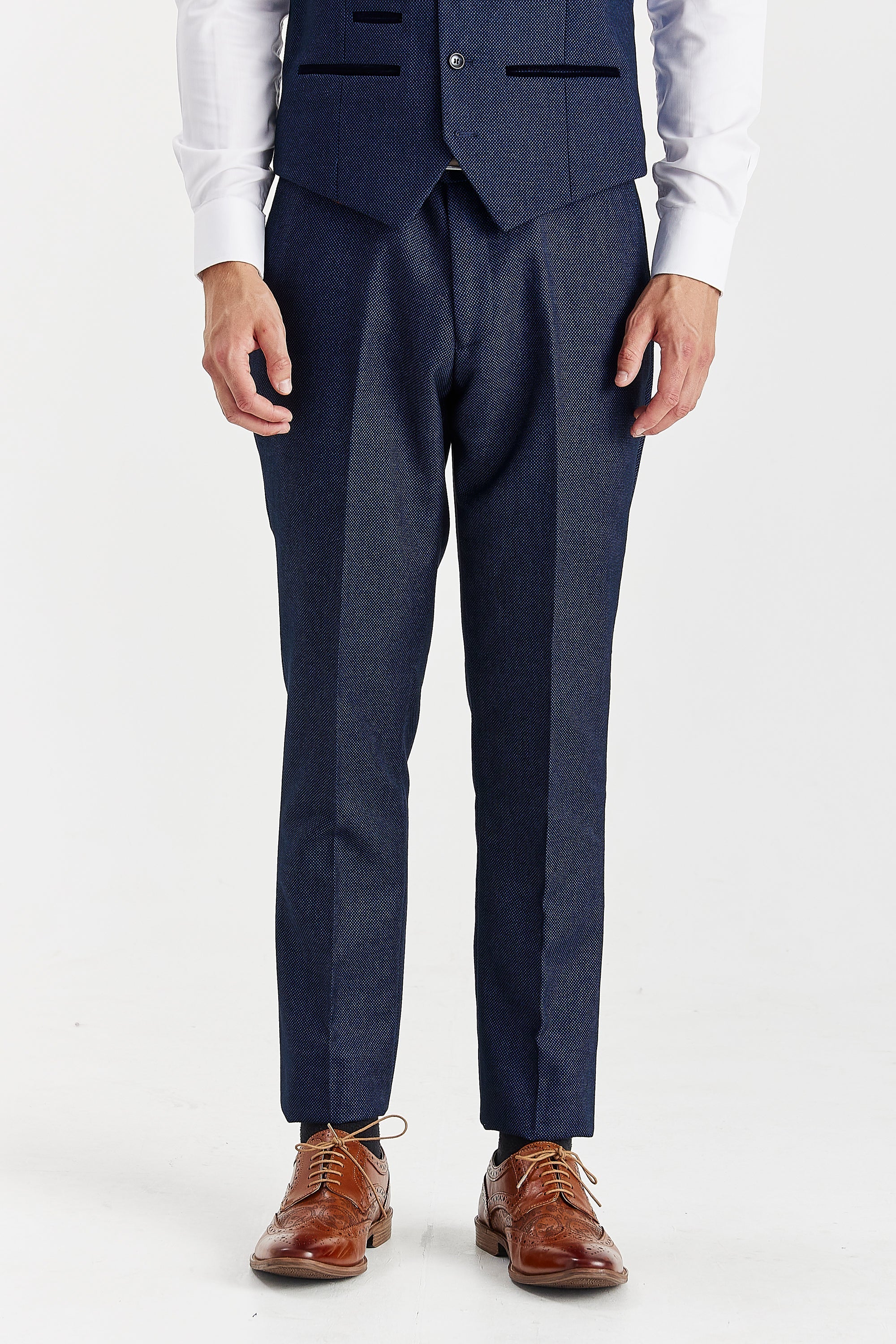 Close-up front view of men's slim-fit navy birdseye suit trousers and matching waistcoat, ending in brown leather brogue shoes.