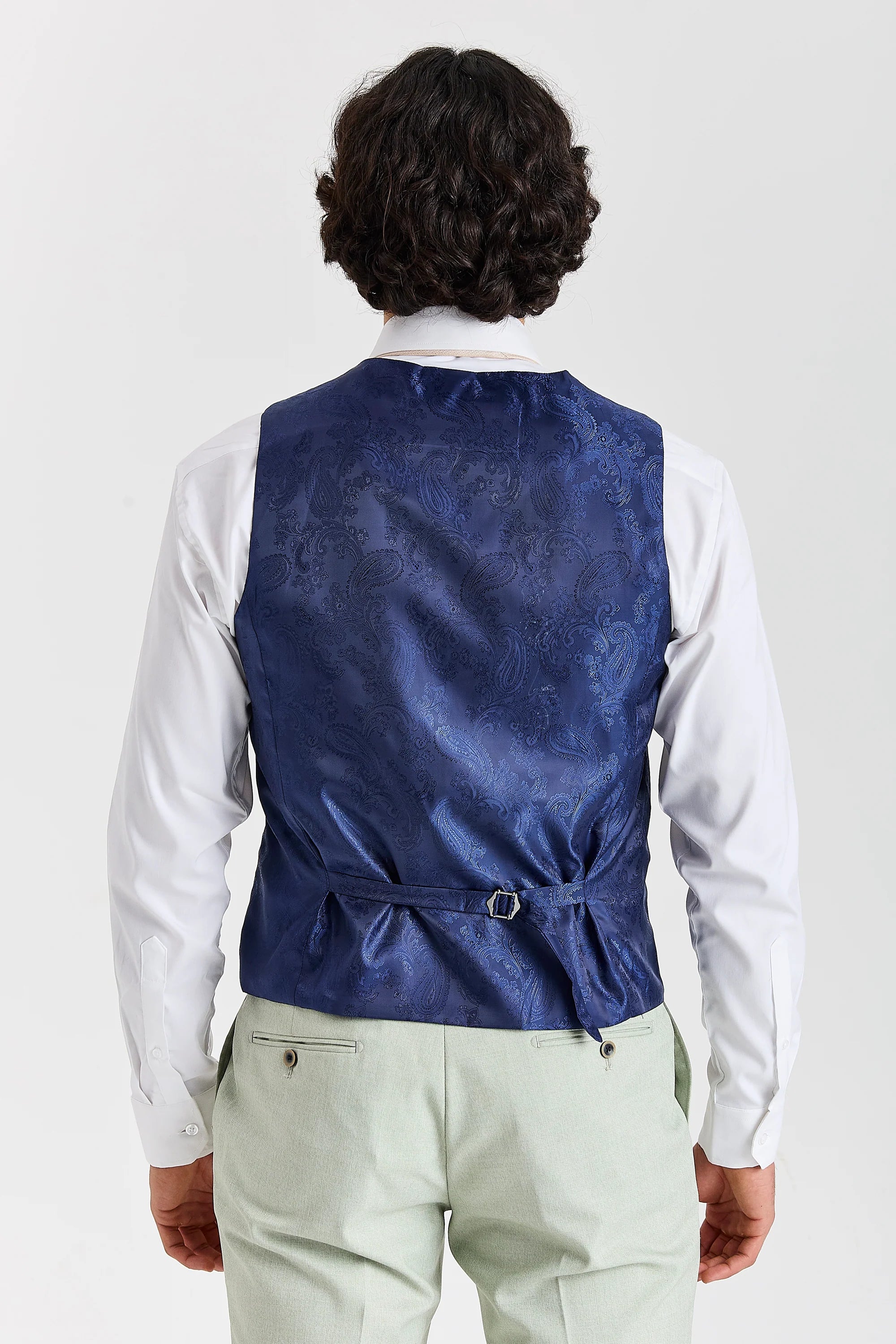 Rear view of the sage waistcoat with a blue paisley back panel and adjustable strap, worn with a white shirt and matching trousers.