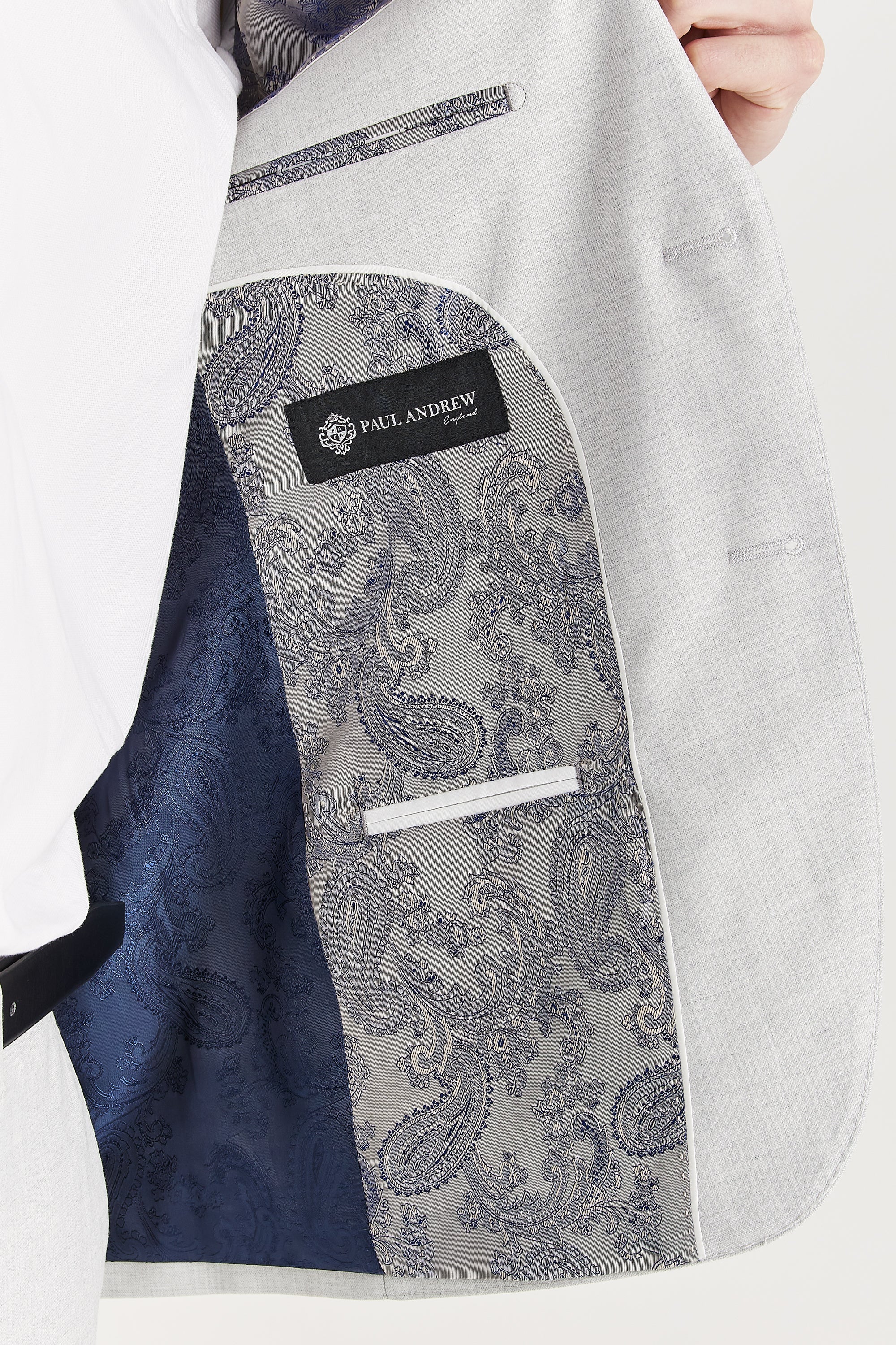 Interior view of a silver suit jacket revealing a distinctive silver and blue paisley lining, white piping, and the Paul Andrew brand label.