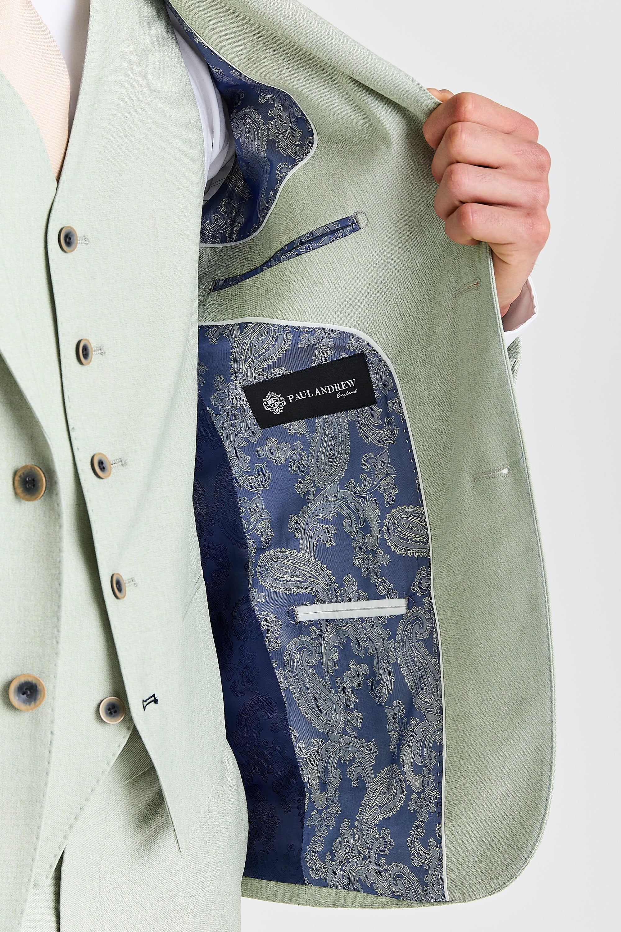 Detail view of a mint green suit jacket showing blue silver and navy paisley lining, inner pocket, contrast piping and Paul Andrew label.