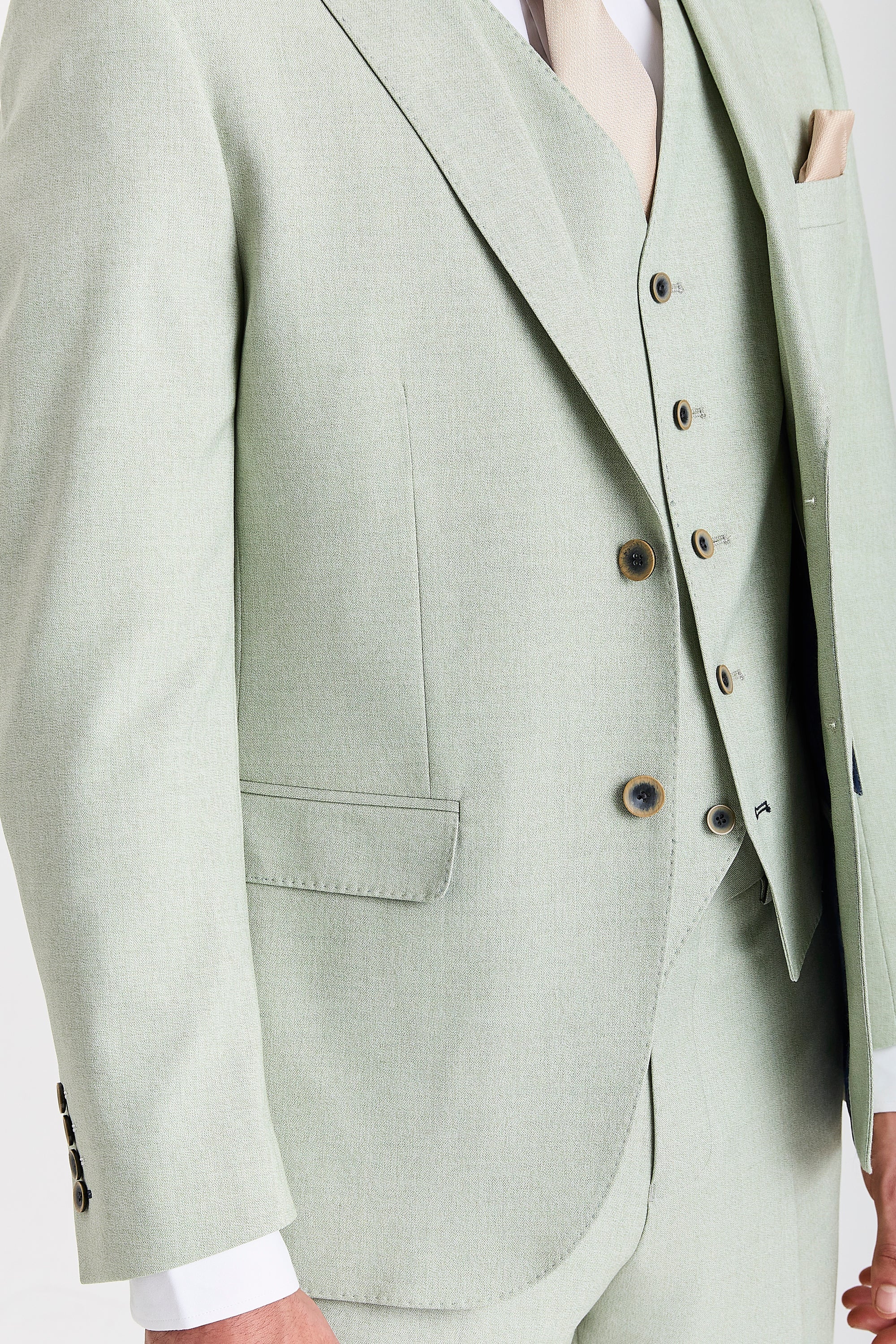 Close-up of a mint green suit jacket and waistcoat showing textured fabric, contrast buttons, pocket flap and cream tie.