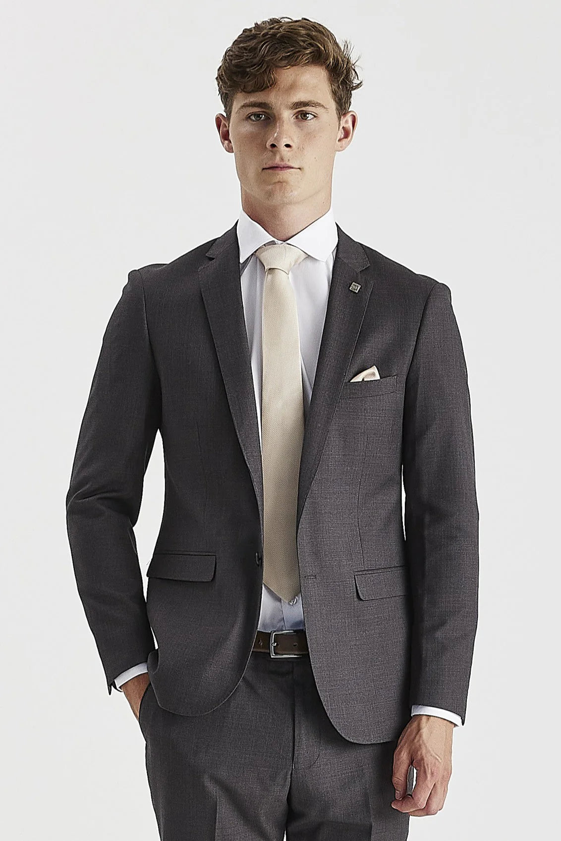 Waist-up front view of a man wearing a tailored charcoal grey men's suit jacket, styled with a white shirt, light beige tie, and matching pocket square.