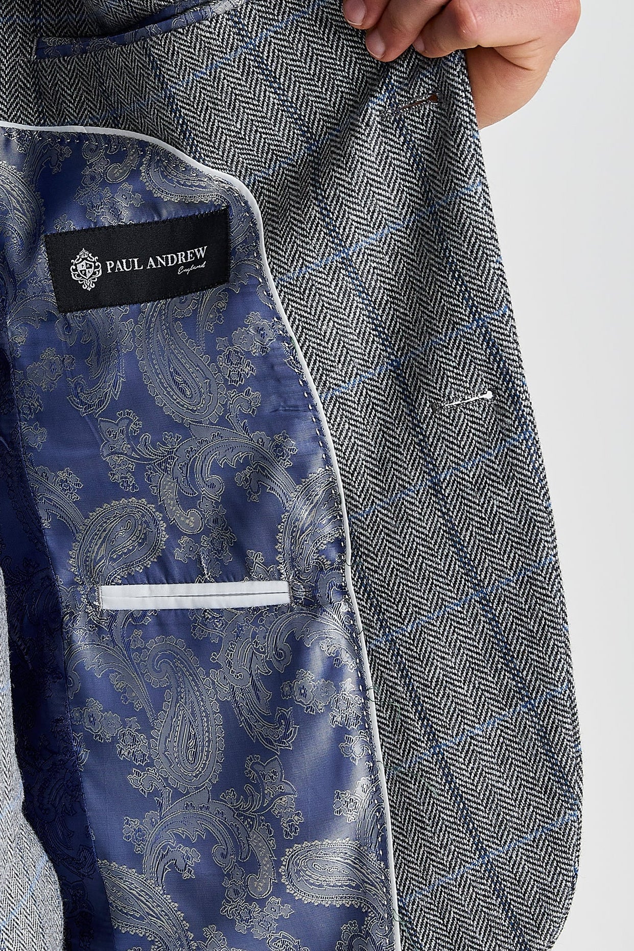Interior view of the grey herringbone tweed check blazer with blue paisley lining and a visible Paul Andrew logo label.