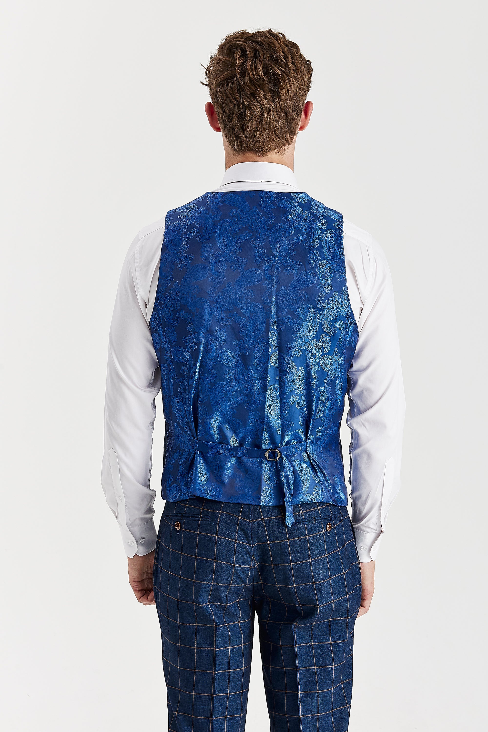 Rear view of the navy waistcoat with a blue paisley back panel and adjustable strap, worn with a white shirt and matching windowpane trousers.
