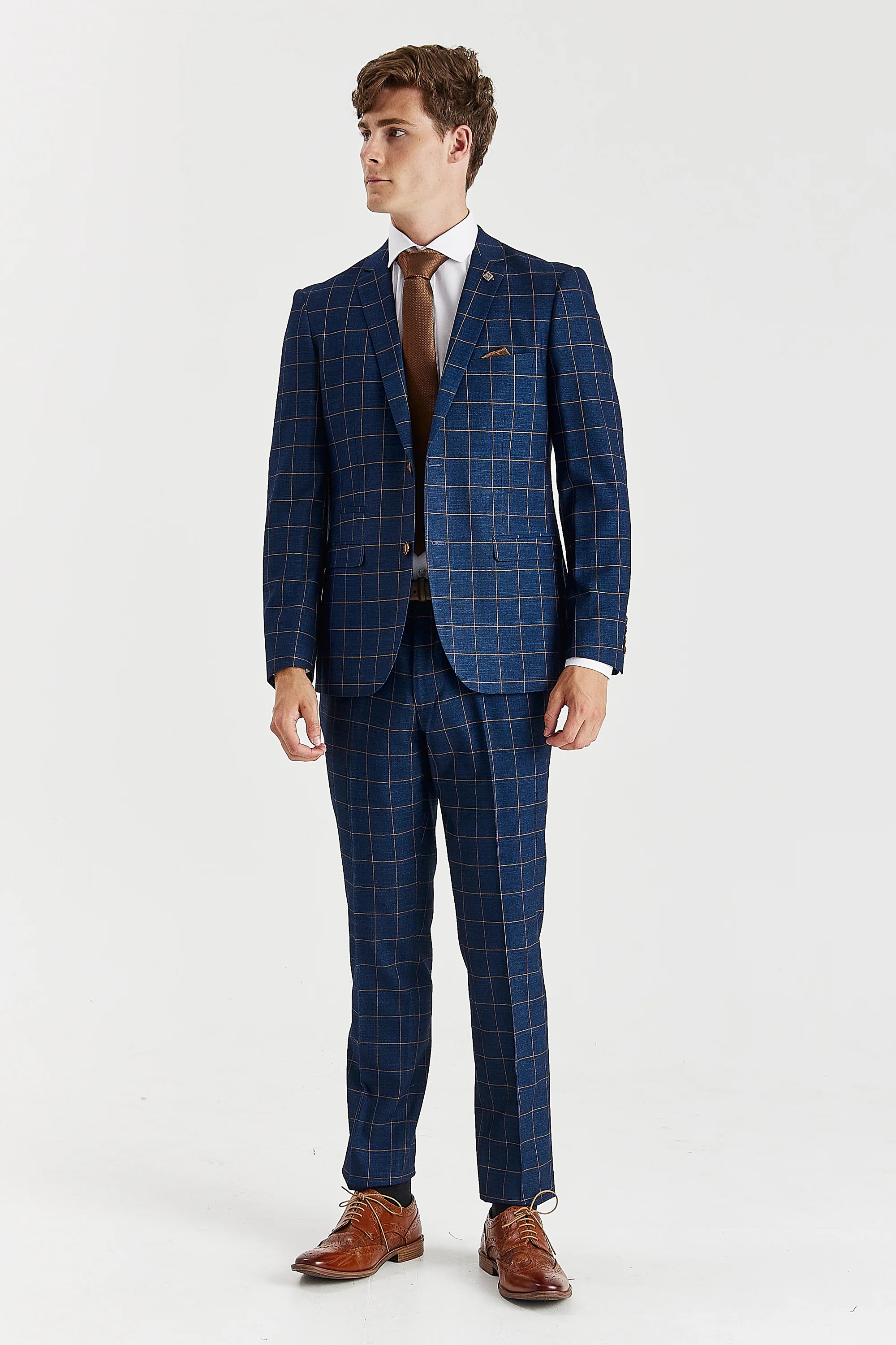 Full-length front view of a man wearing a tailored navy suit featuring brown windowpane checks, styled with a crisp white shirt, brown tie, and brown leather brogue shoes