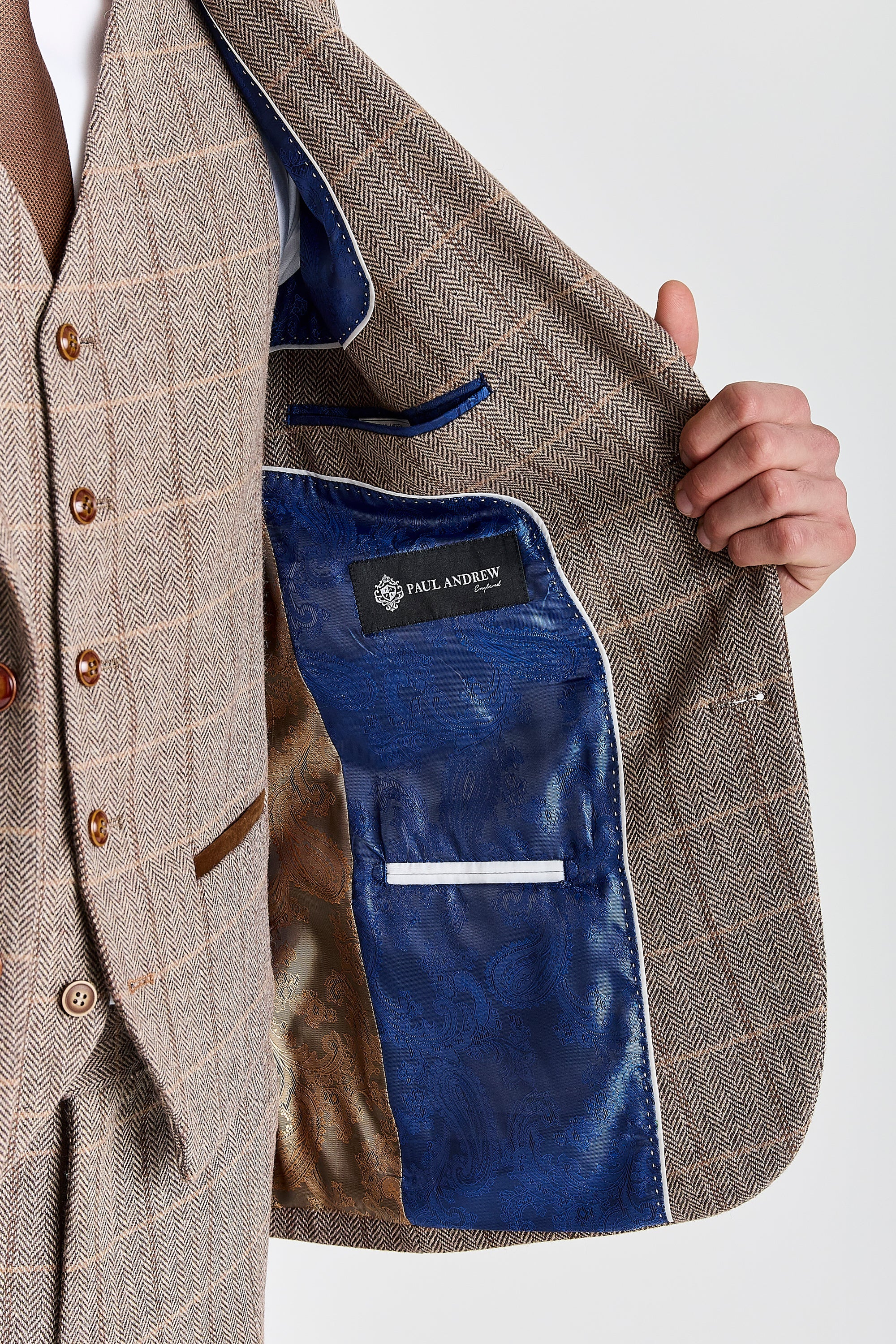 Detail view of a Harris brown herringbone tweed suit jacket interior with blue and brown paisley lining, white piping, inner pockets and Paul Andrew label.