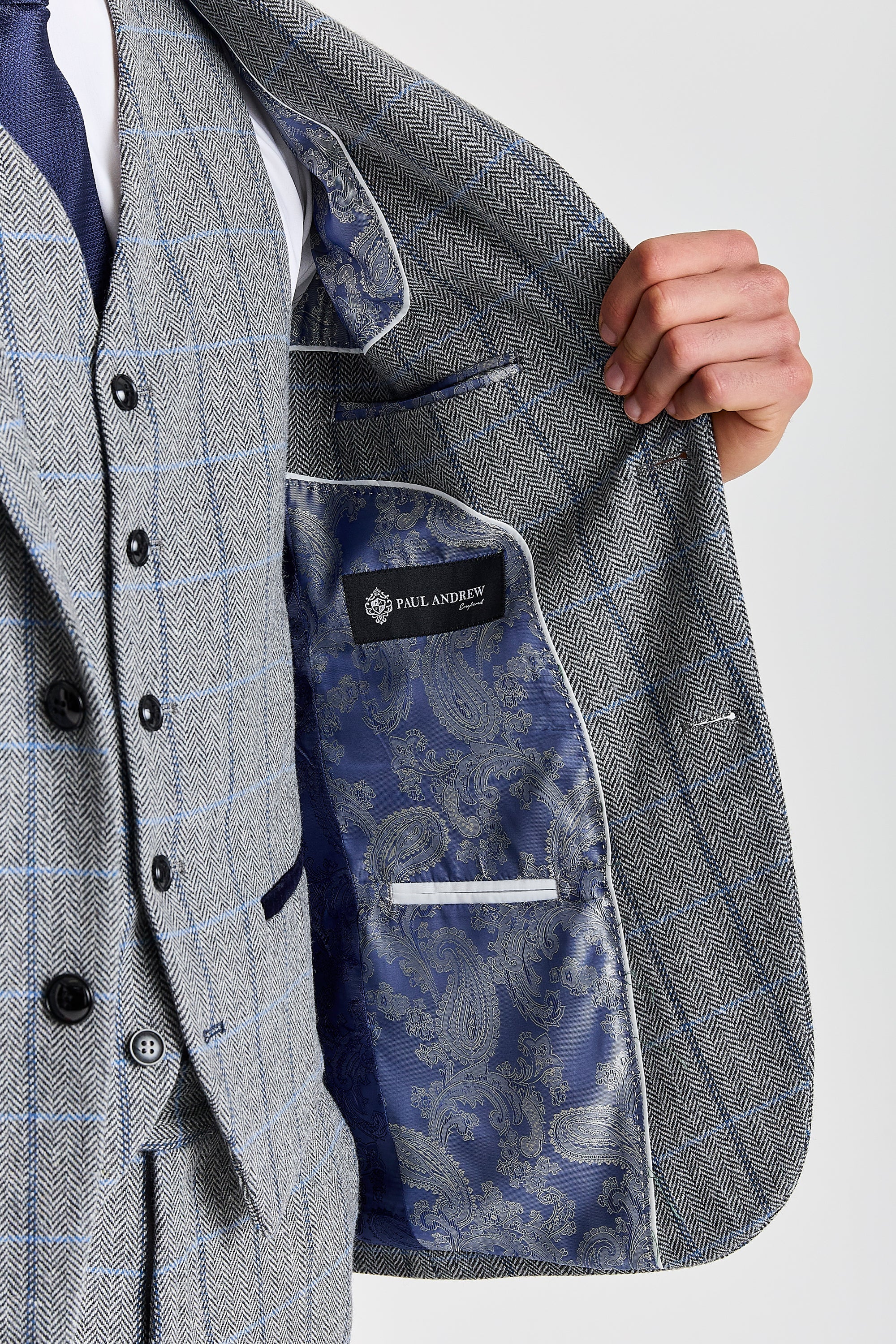 Detail view of a Harris grey herringbone tweed suit jacket interior with blue and navy paisley lining, white piping, inner pockets and Paul Andrew label.