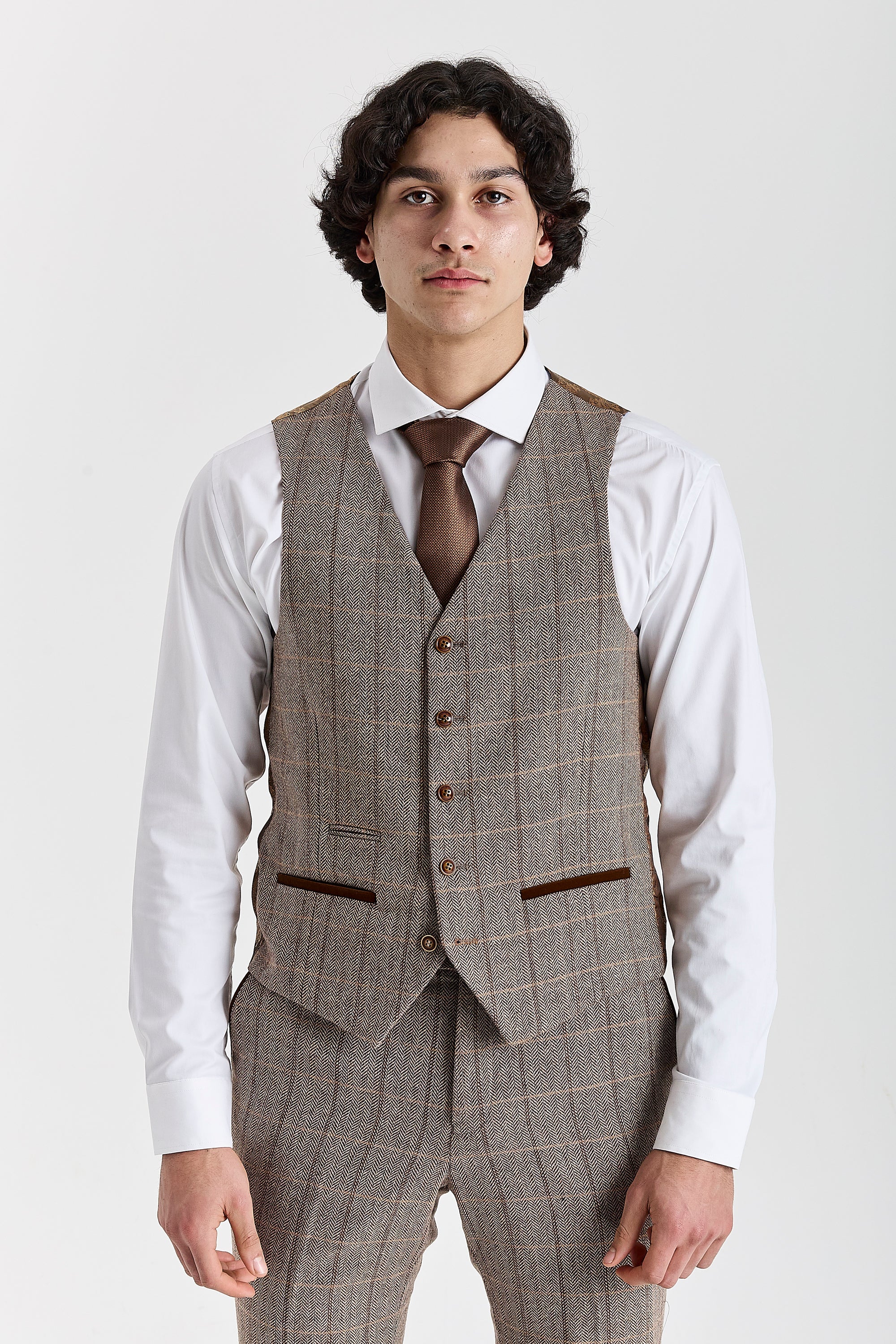 Front view of the brown herringbone tweed waistcoat with brown buttons and suede pocket trimmings, worn with matching trousers, a white shirt and a brown tie.