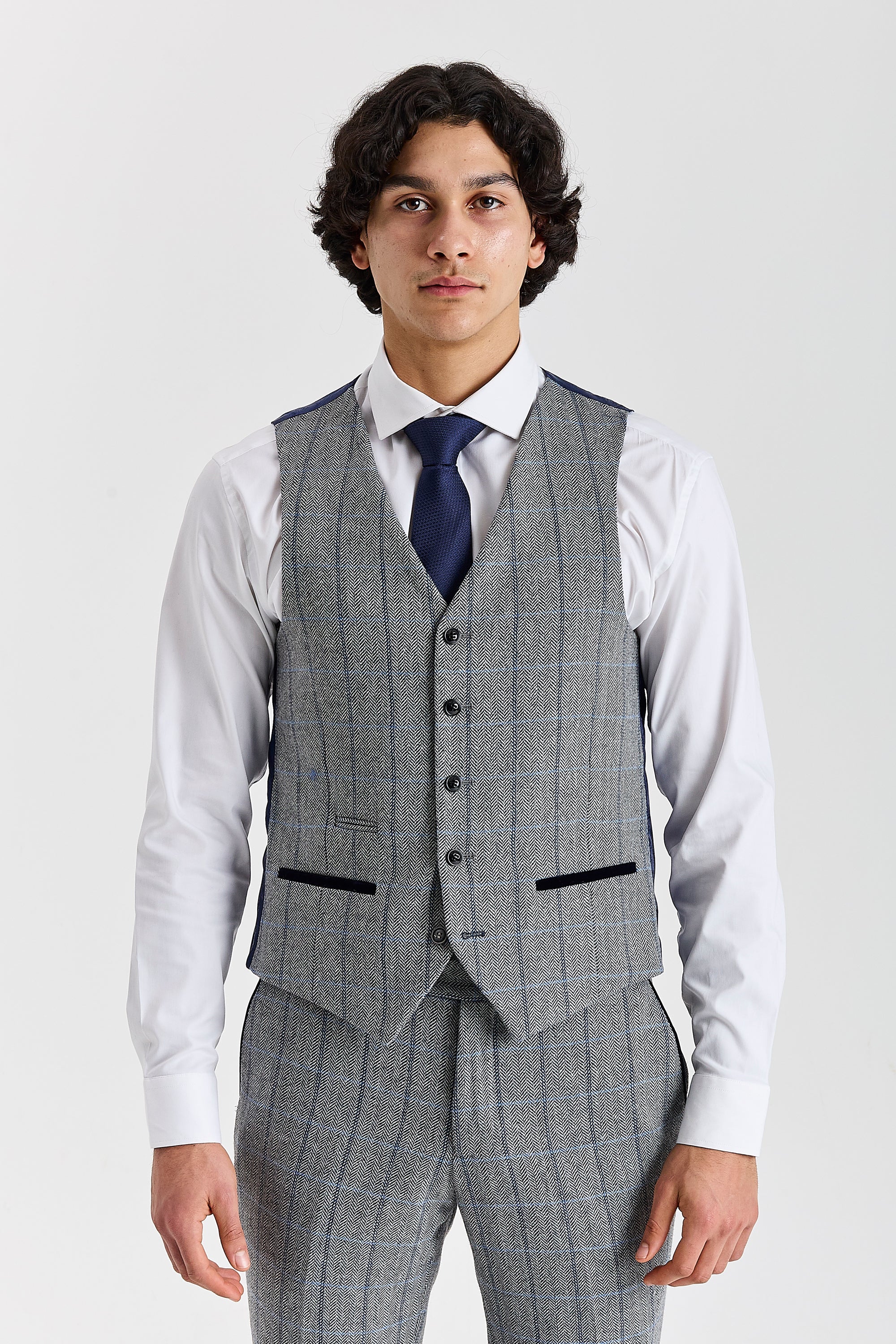 Front view of the grey herringbone tweed waistcoat with contrast pocket trimmings, worn with matching trousers, a white shirt and a navy tie.