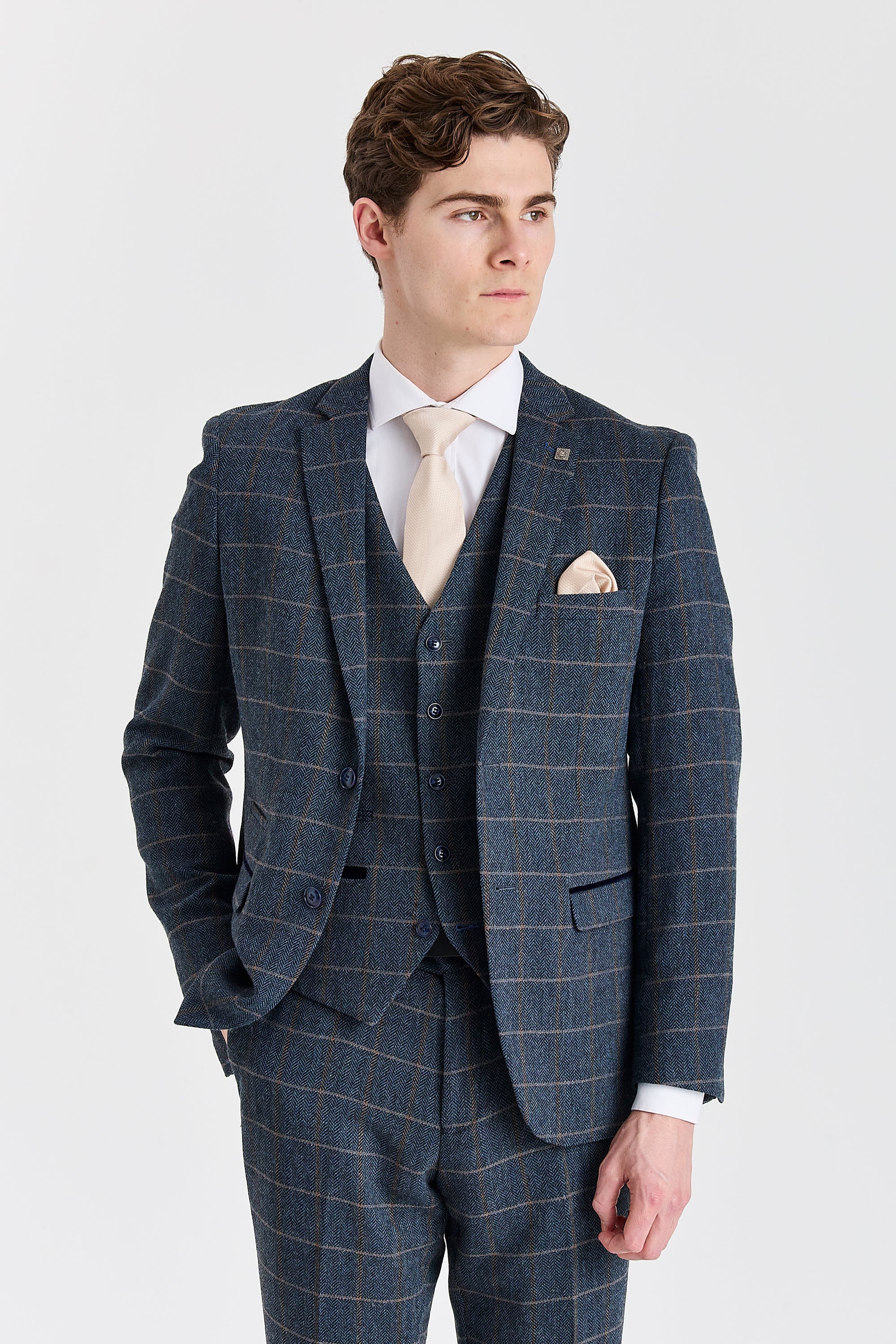 Front view of a man wearing a Harris navy herringbone tweed three piece suit with a tan windowpane check, cream tie and matching waistcoat.