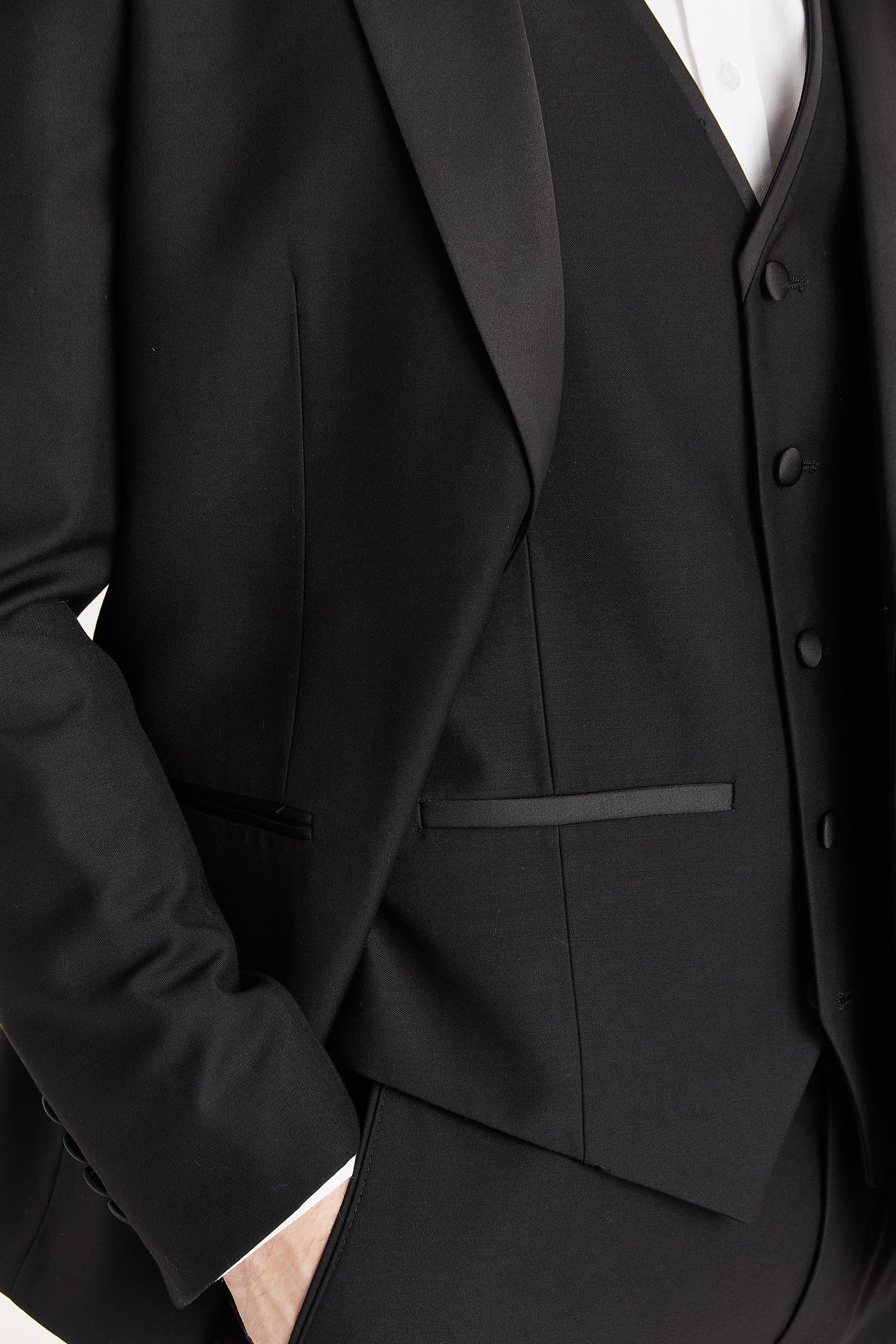 Detail view of a black dinner suit jacket and waistcoat, showing a satin peak lapel, black buttons and pocket trim.