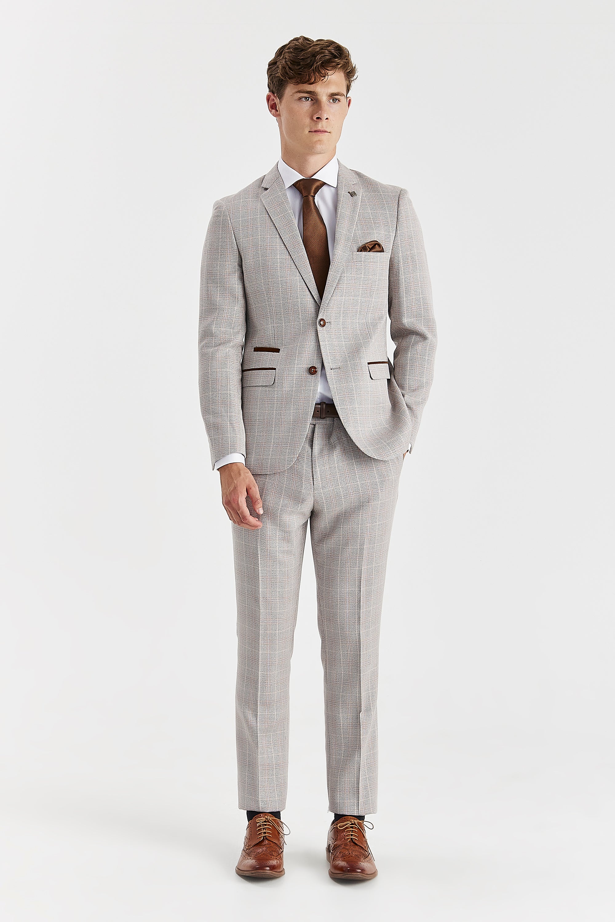 Men’s beige trousers shown as part of a full outfit with the matching blazer, white shirt, brown tie and brown brogues.