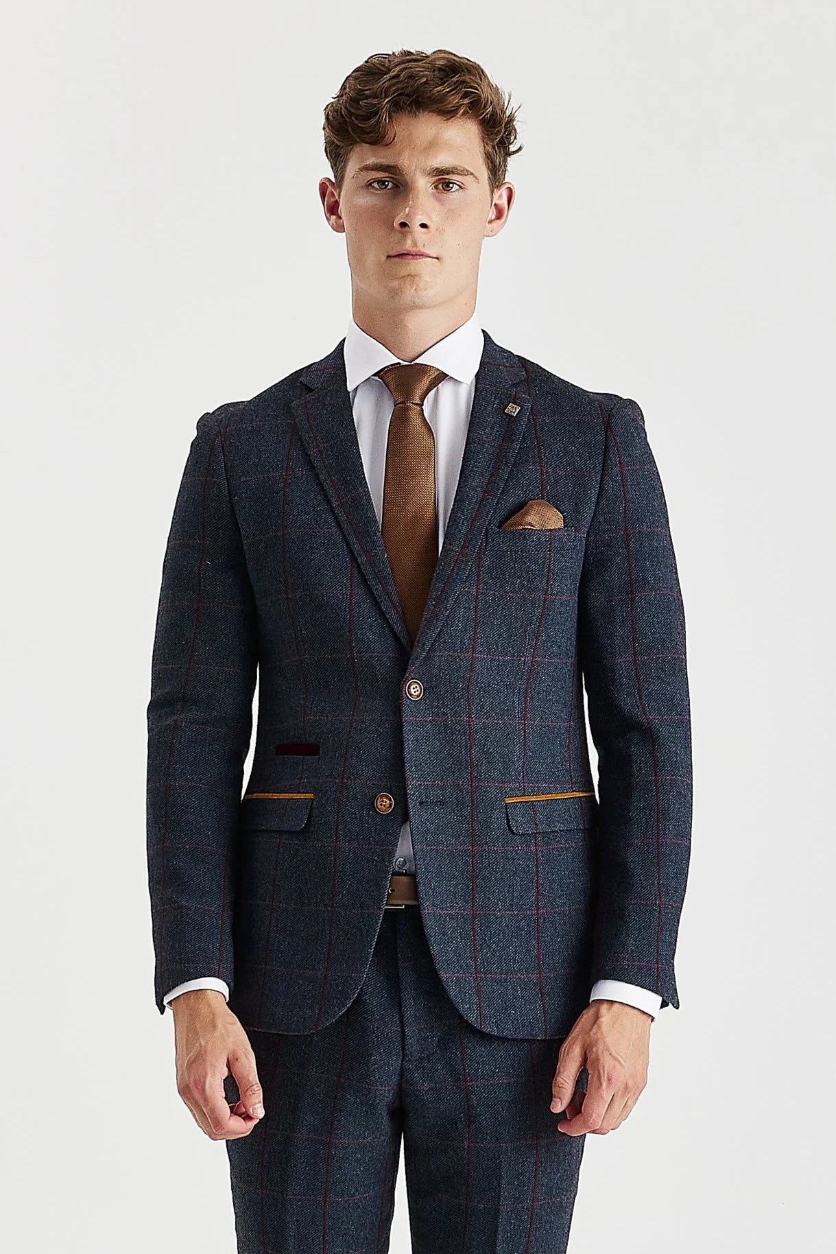Knee-up view of a man wearing a navy tweed suit blazer and trousers with a burgundy check, a white shirt, and a brown tie.