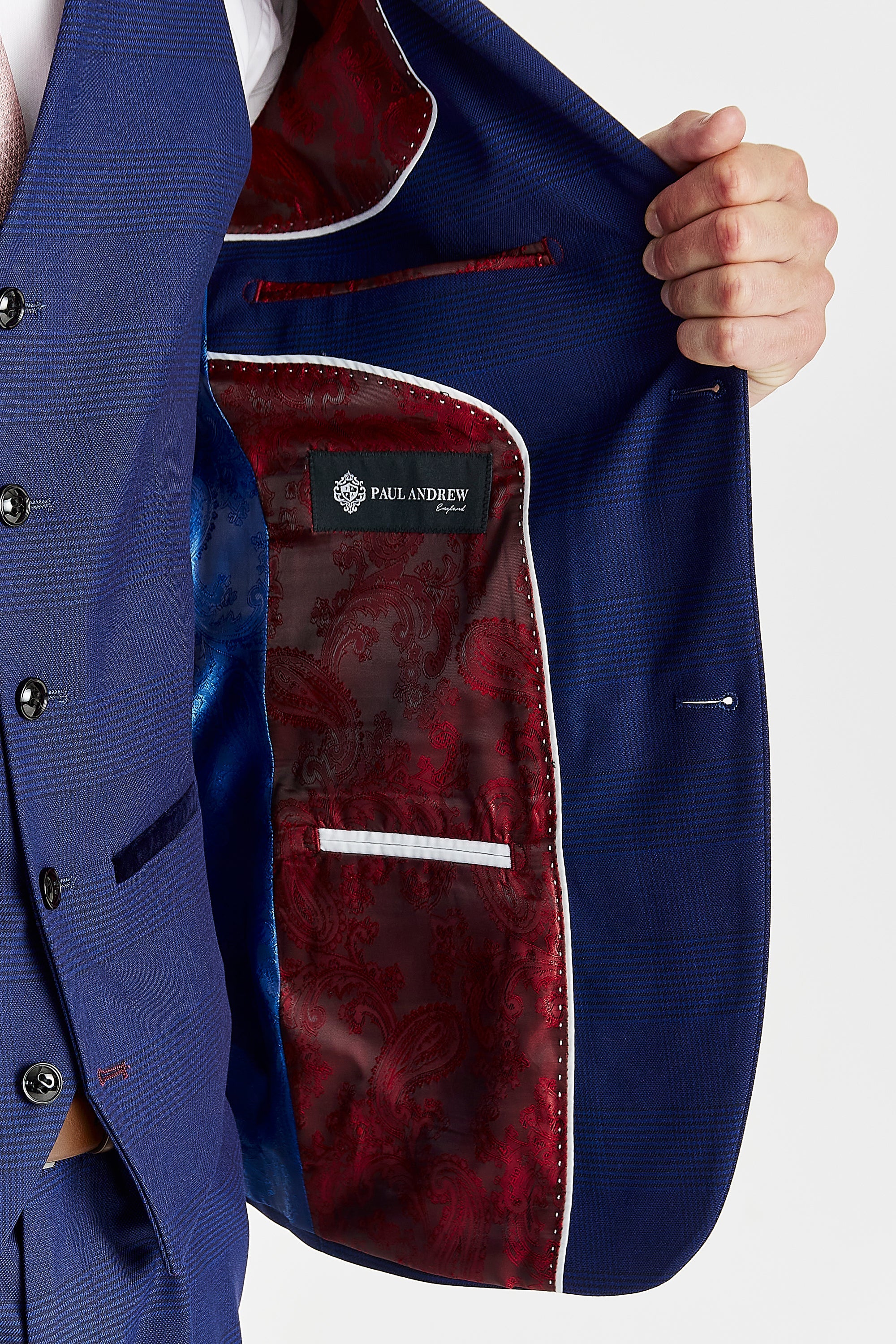 Detail view of a blue glen check suit jacket interior with red and blue paisley lining, white piping, inner pockets and a Paul Andrew label.