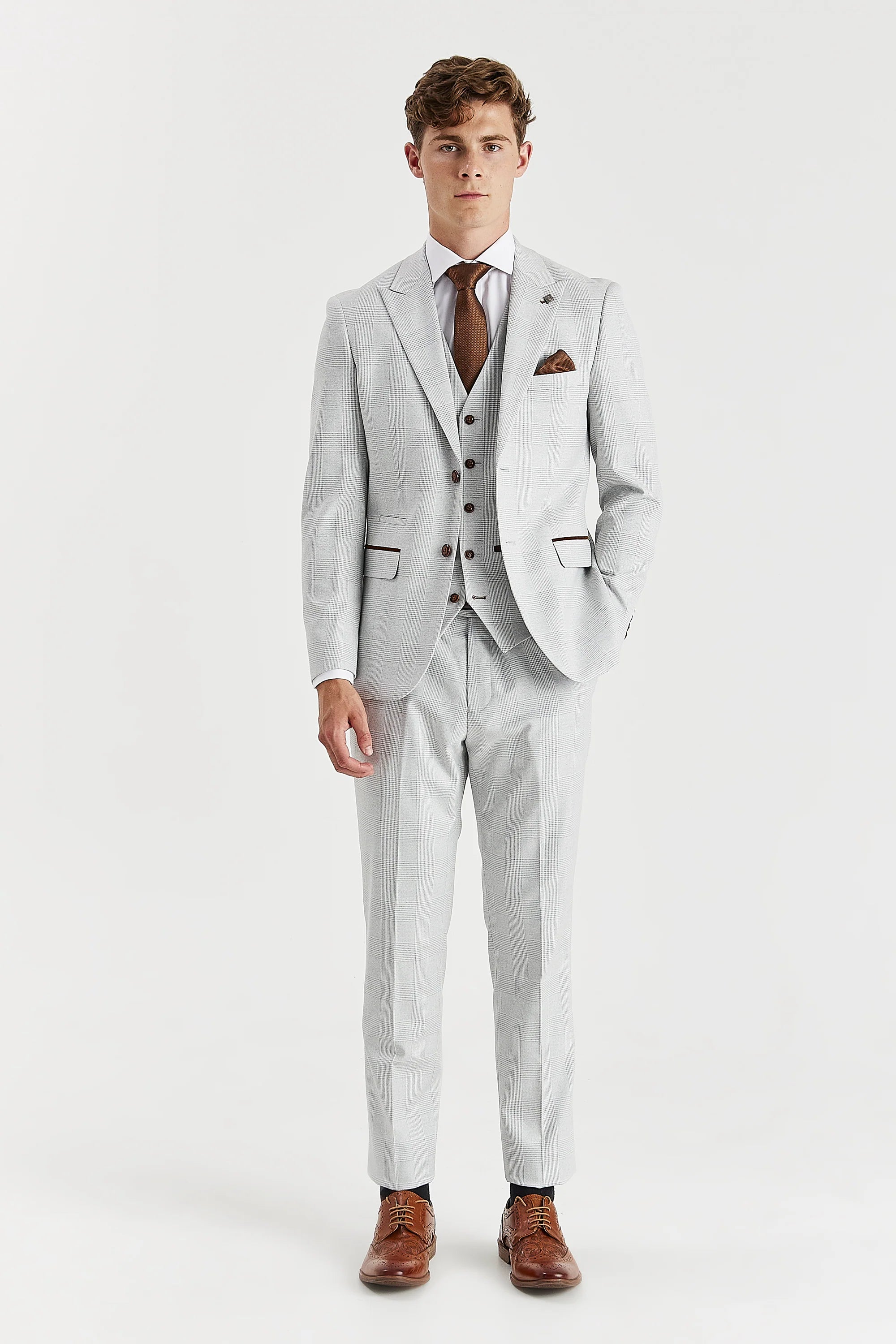 Full-length front view of a man wearing a stone three piece suit with a glen check pattern, jacket, waistcoat, trousers, white shirt, brown tie and brown shoes.
