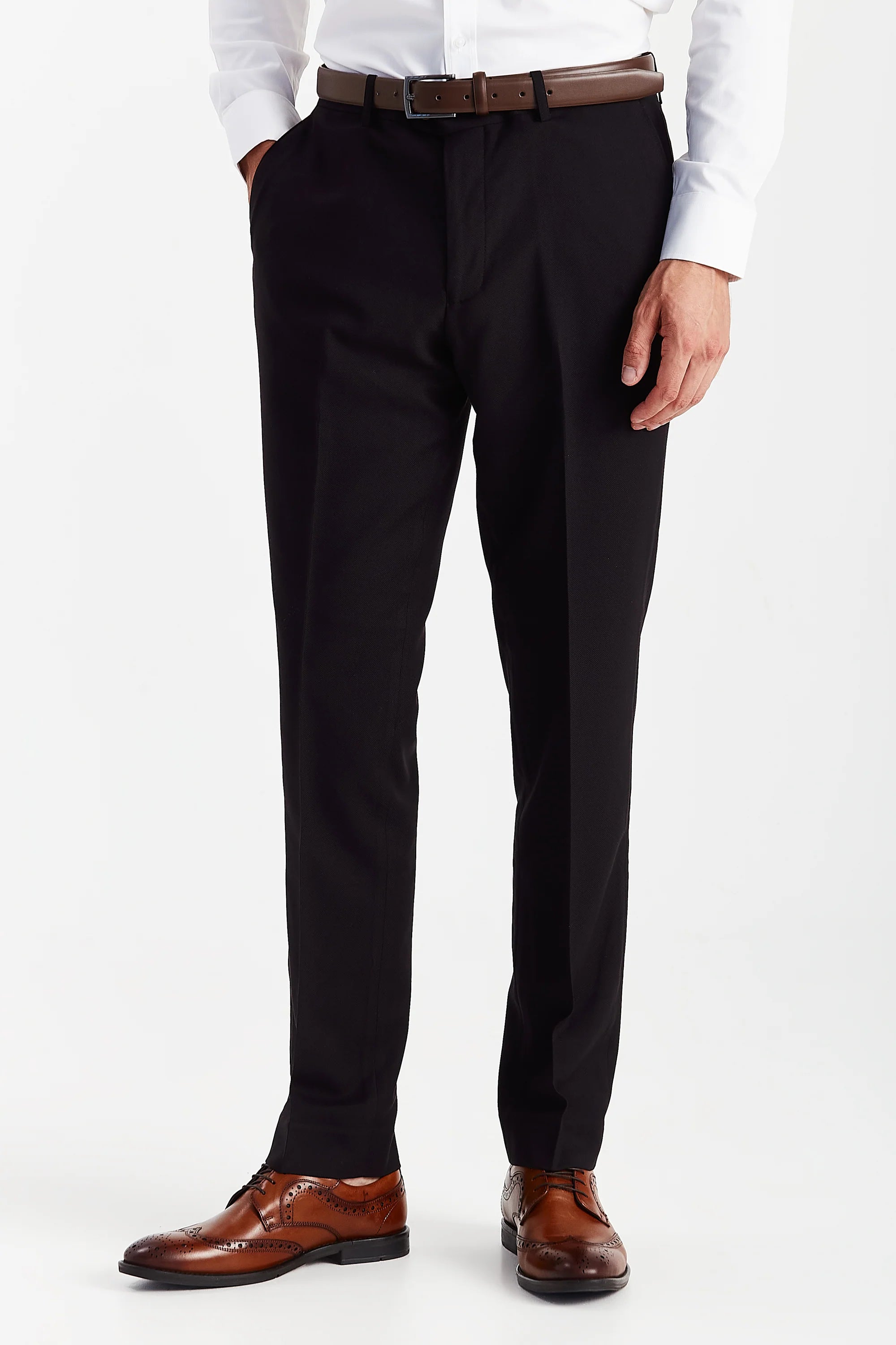 Front view of black textured suit trousers with a brown belt, white shirt cuffs and brown brogue shoes.