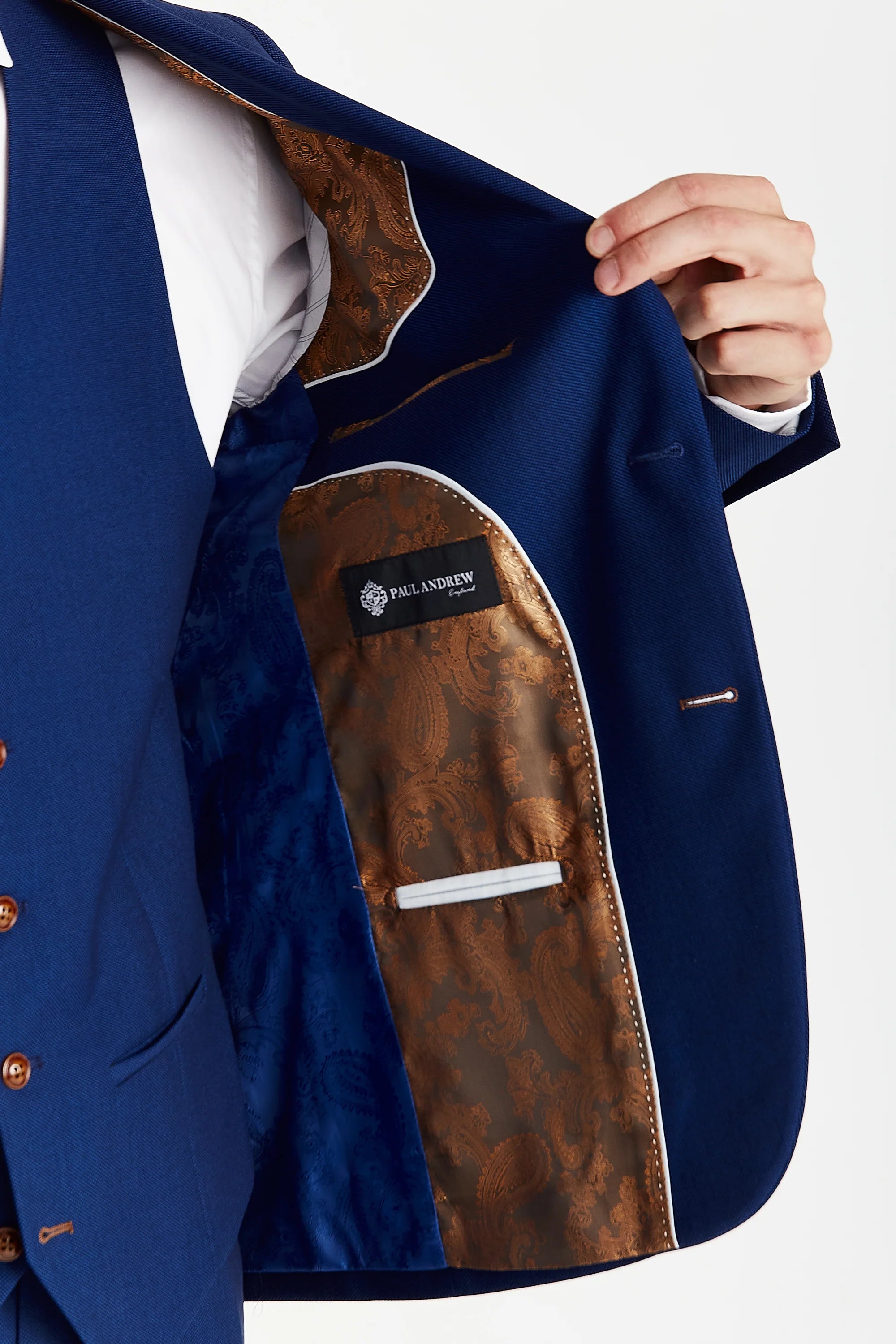 Detail view of a blue textured suit jacket interior with brown and blue paisley lining, white piping, inner pockets and a Paul Andrew label.