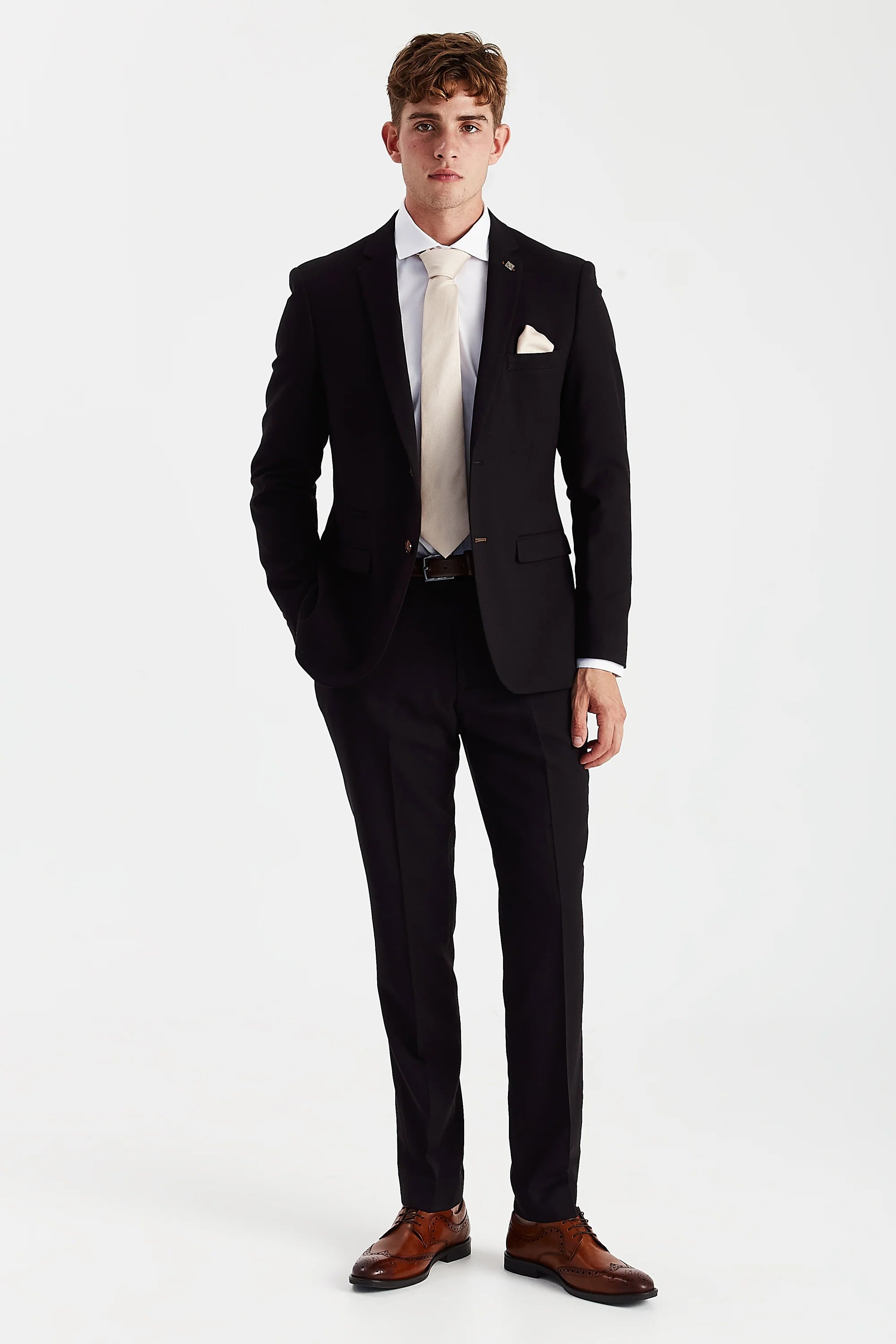 Full front view of black textured two-piece suit worn with a white shirt, cream tie and brown brogues