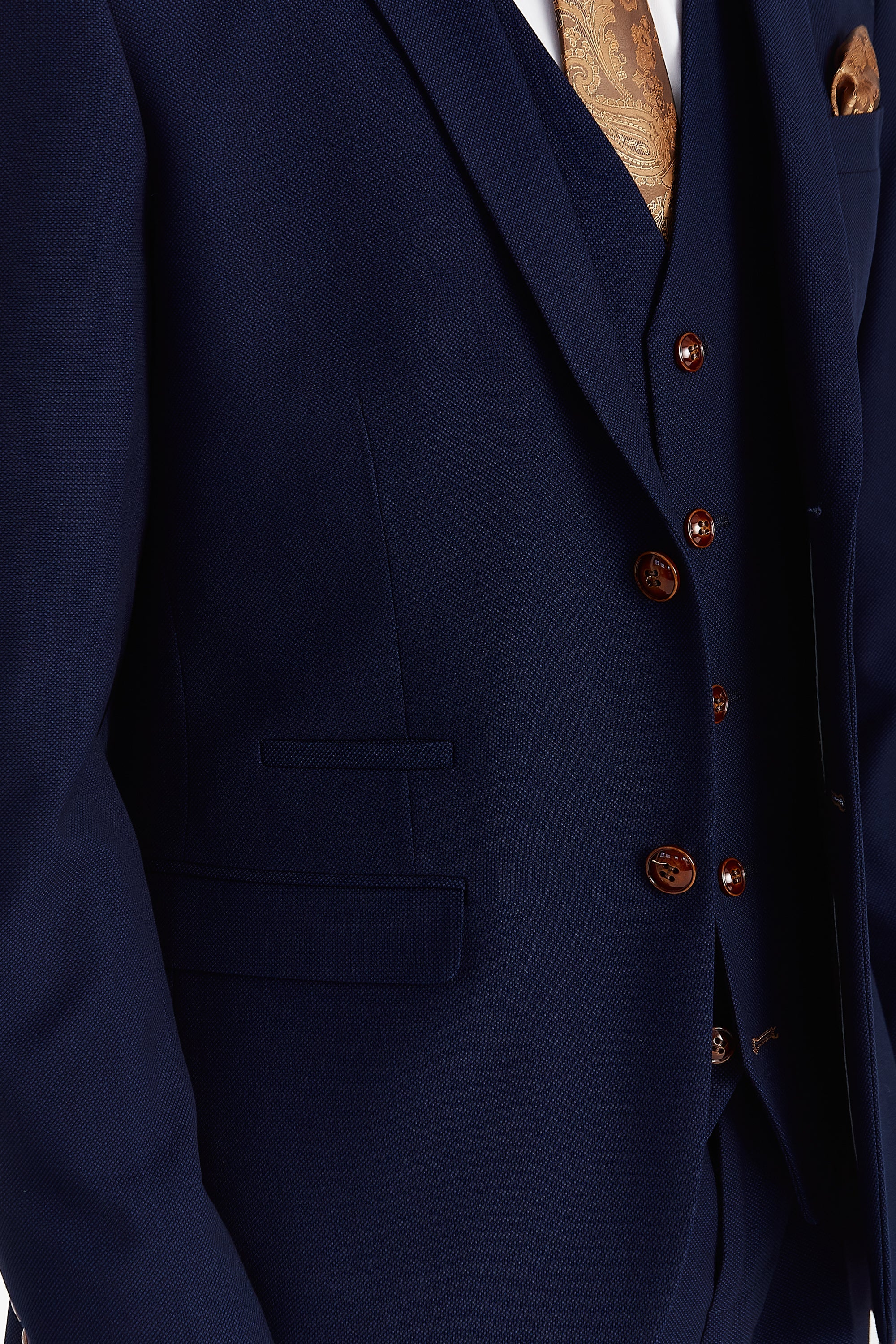Close-up detail of a navy textured suit jacket and waistcoat with brown buttons and a gold paisley tie.