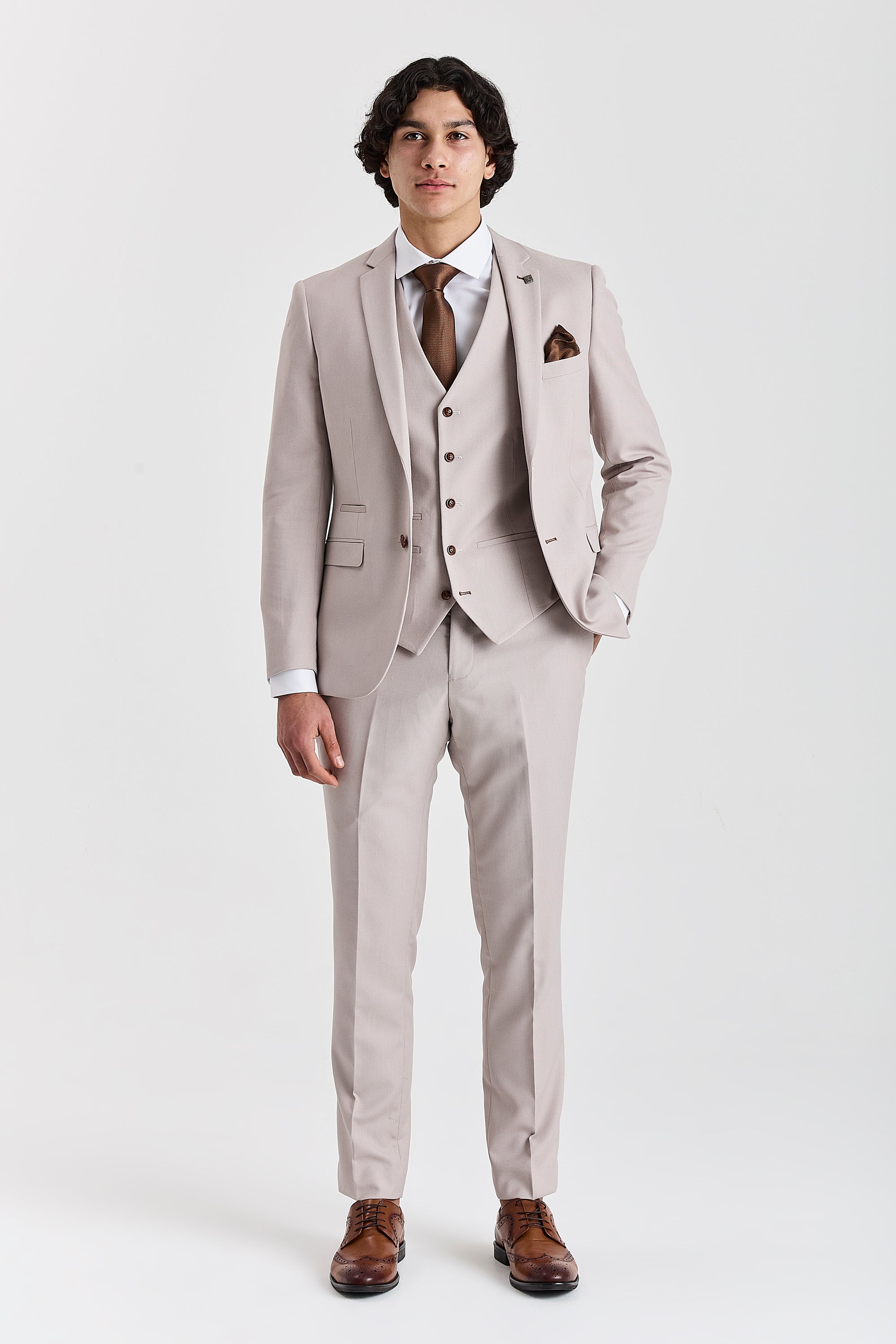 Full-length front view of a man wearing a stone textured three piece suit with a white shirt, brown tie, matching pocket square and brown brogue shoes.