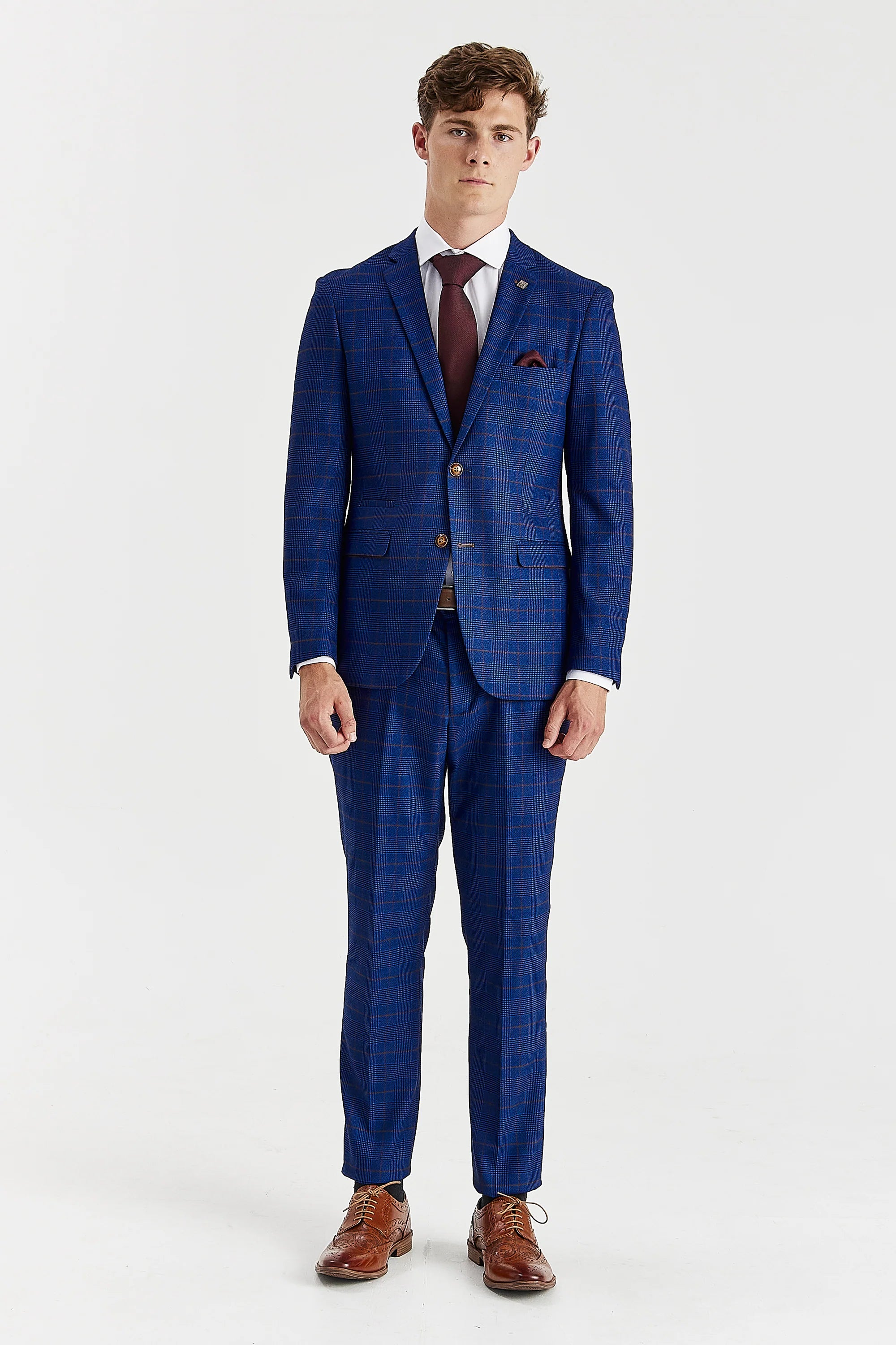 Full-length front view of a man modeling a navy blue glen check two-piece suit. The slim-fit suit is styled with a white shirt, burgundy tie, and brown leather brogue shoes.