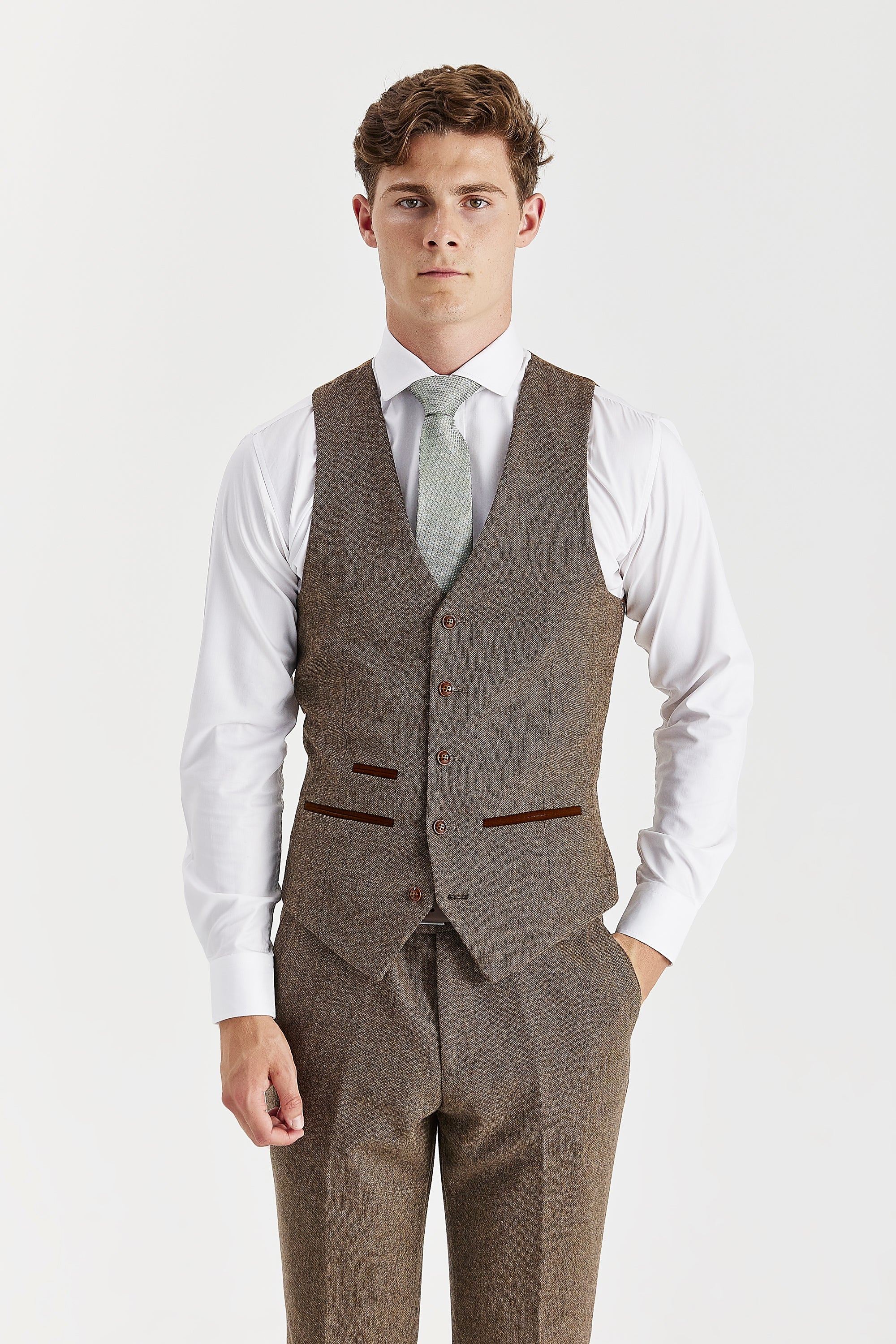 Front view of the brown tweed waistcoat with suede pocket trimmings, worn with matching trousers, a white shirt and a light green tie.