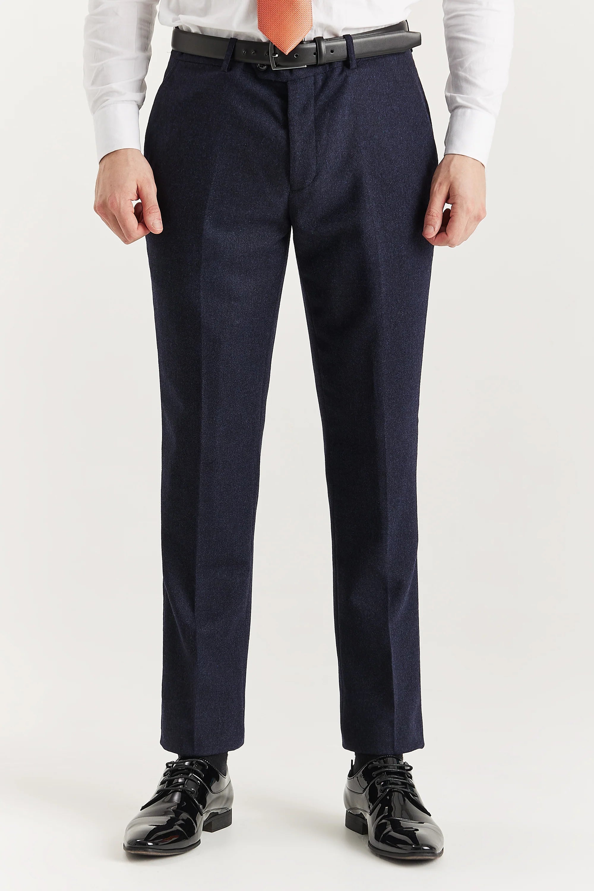 Men’s navy tweed trousers shown from the front, worn with a white shirt, orange tie and black belt and formal shoes.