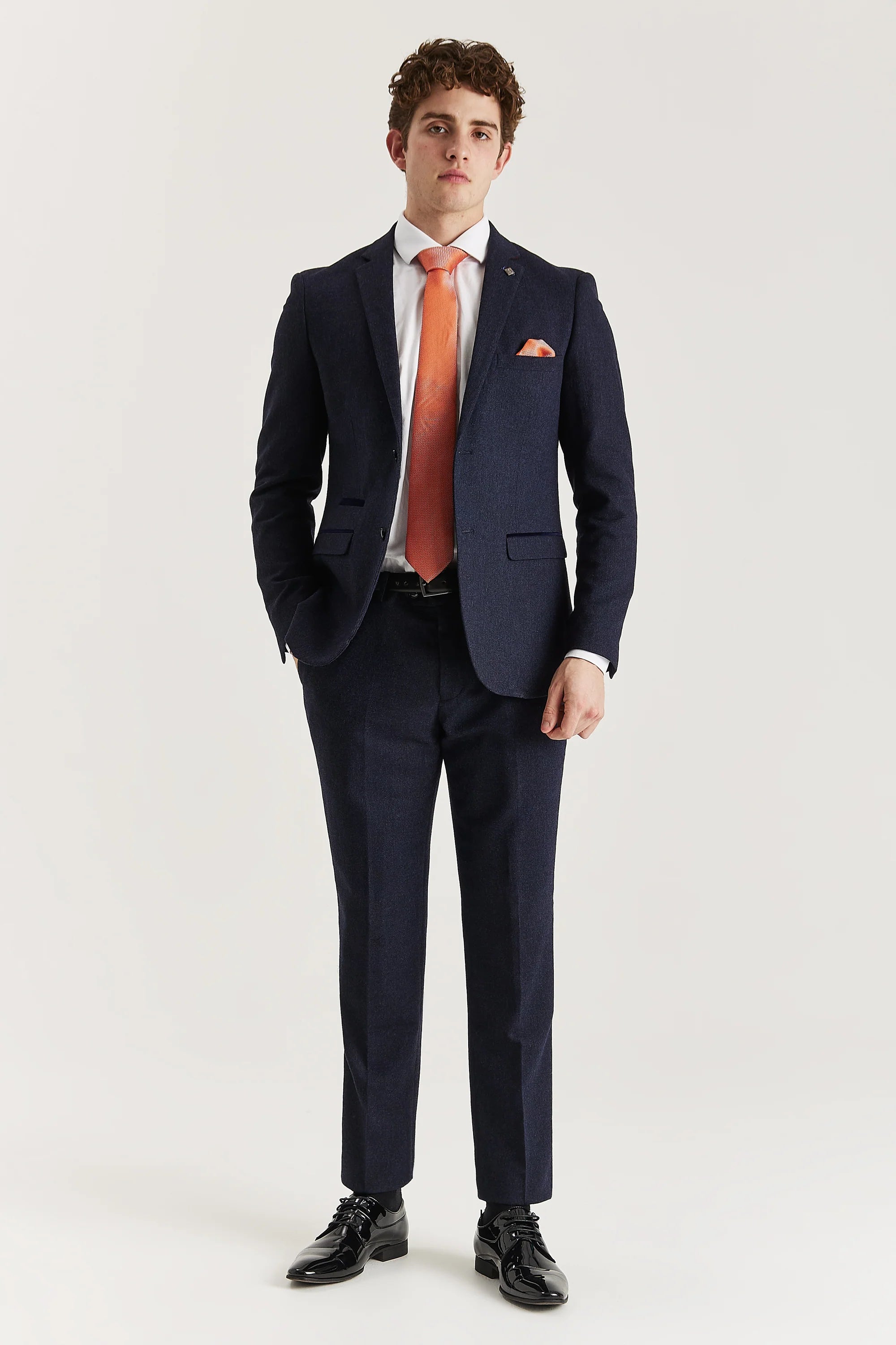 Men’s navy tweed trousers shown as part of a full outfit with the matching blazer, white shirt and orange tie.