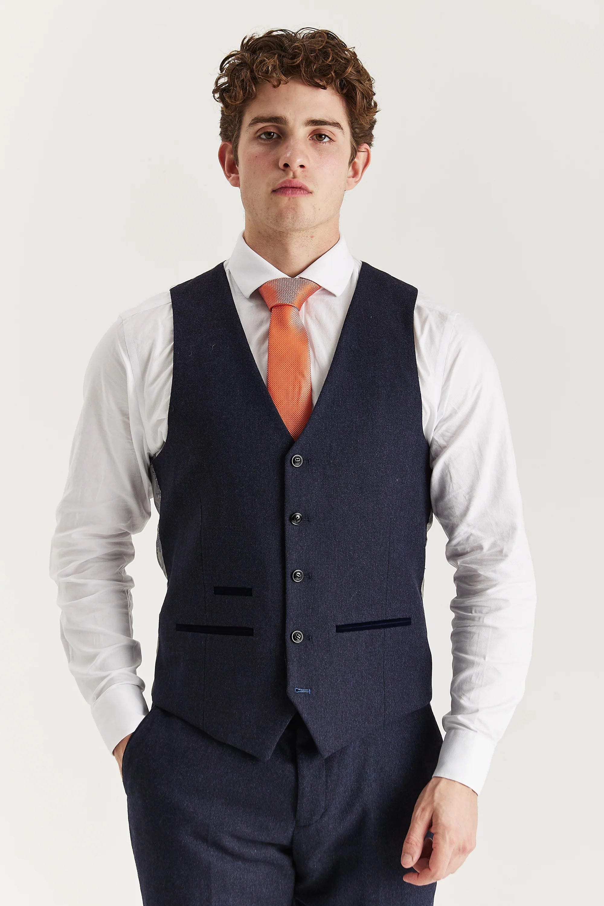 Front view of the navy tweed waistcoat with contrast pocket trimmings, worn with matching trousers, a white shirt and a coral tie.