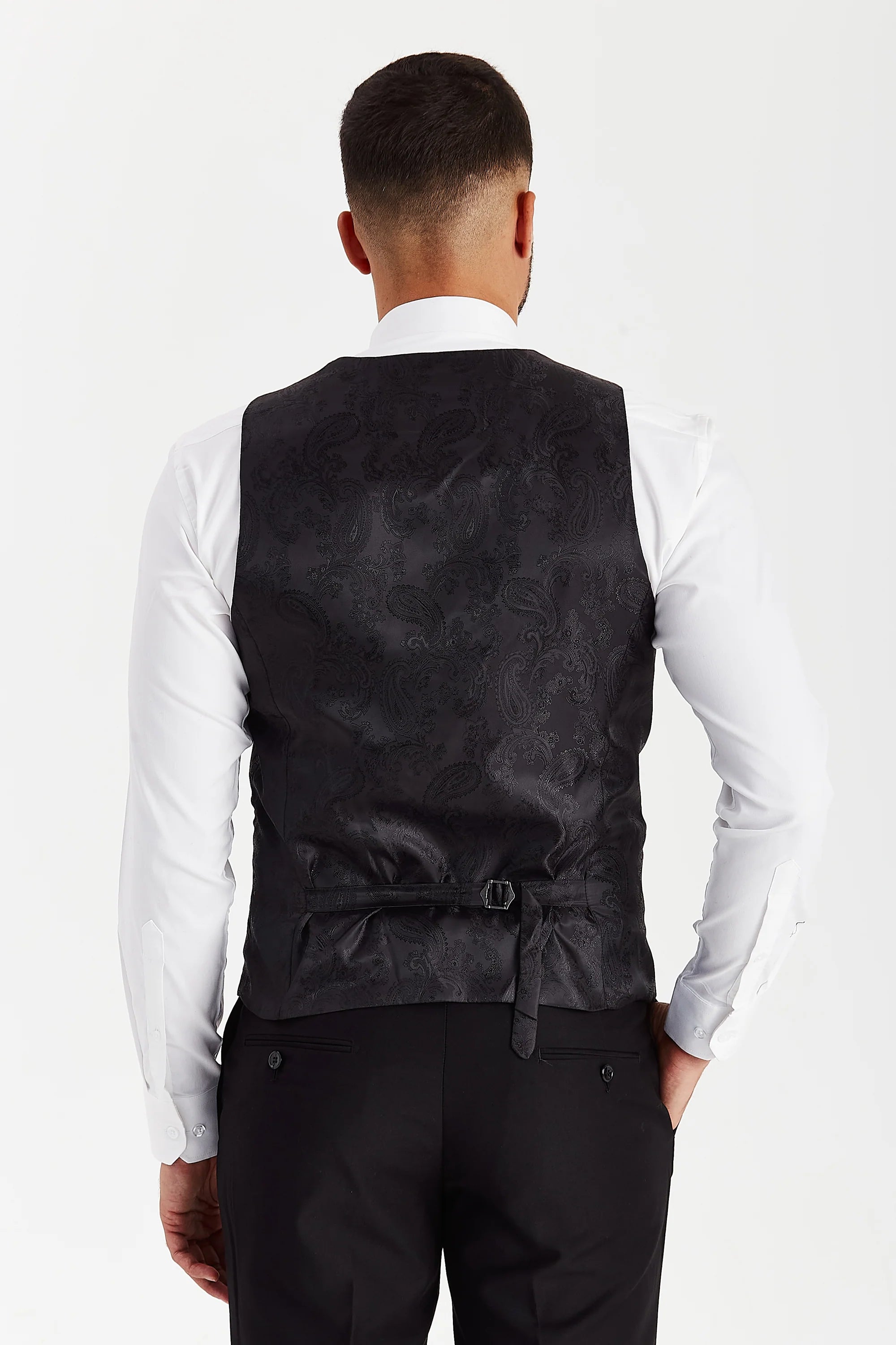 Rear view of the black waistcoat with a black paisley back panel and adjustable strap, worn with a white shirt and black trousers.