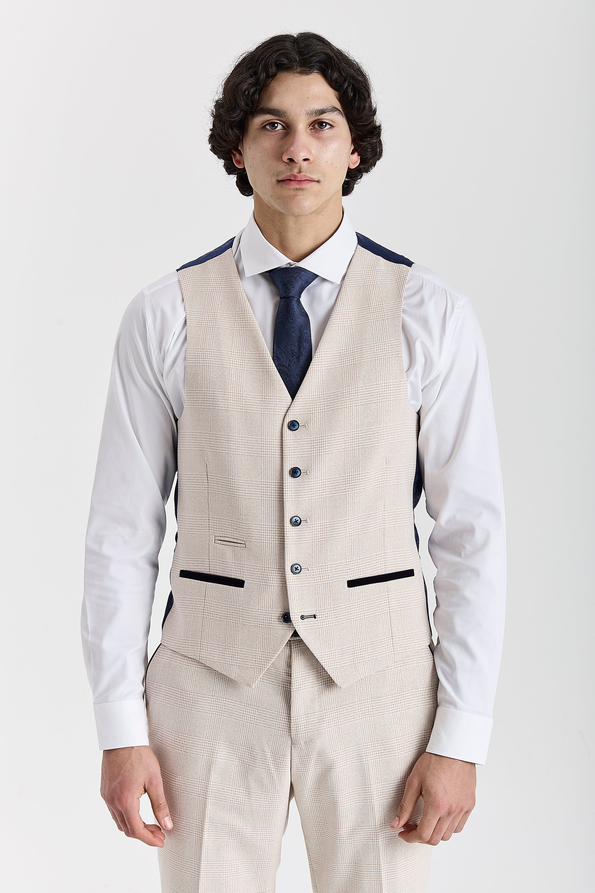 Front view of the cream glen check waistcoat with contrast pocket trimmings, worn with matching trousers, a white shirt and a navy tie.
