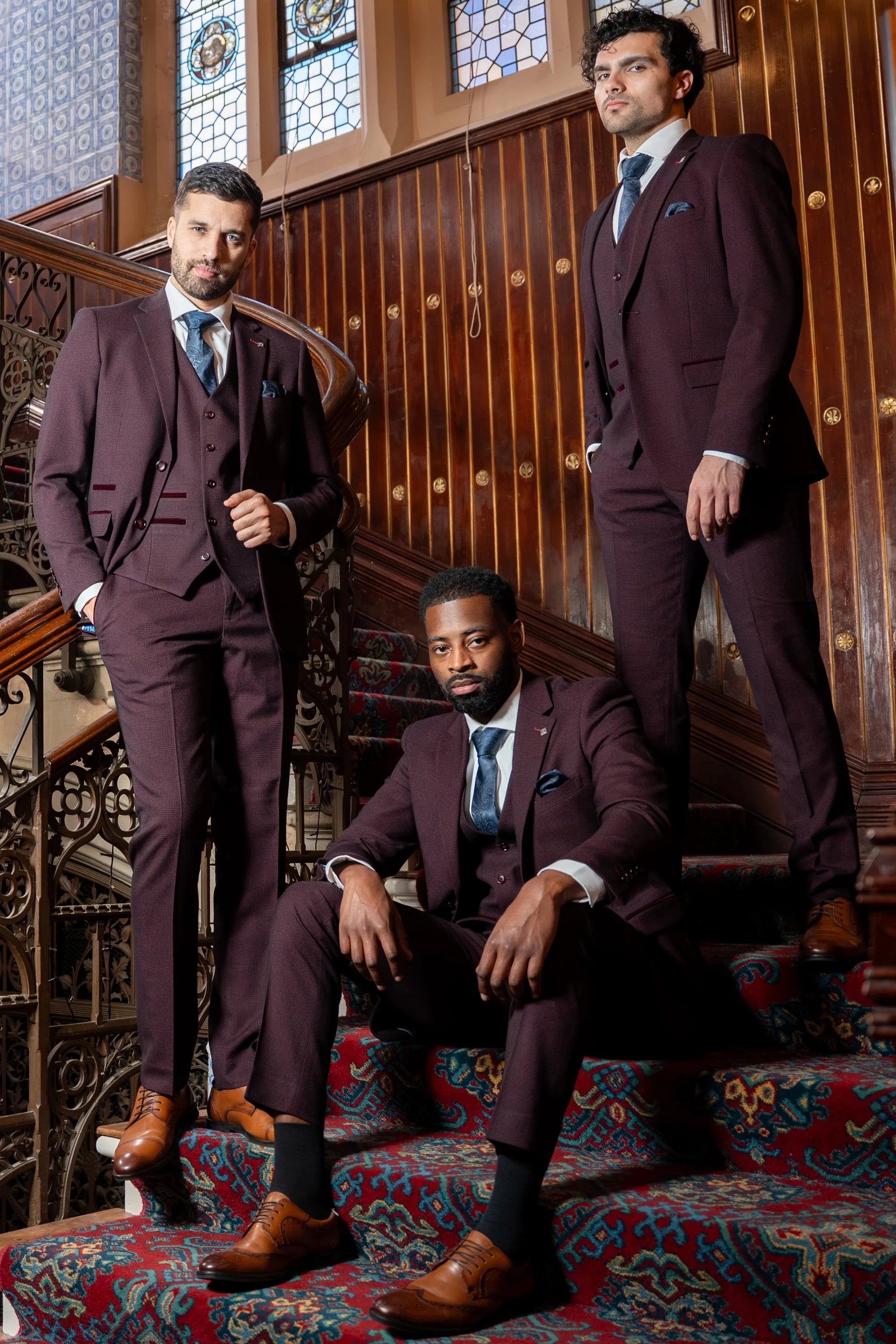 Paul Andrew Regent wine check three piece suit worn by three male models on a staircase with matching waistcoats and blue ties