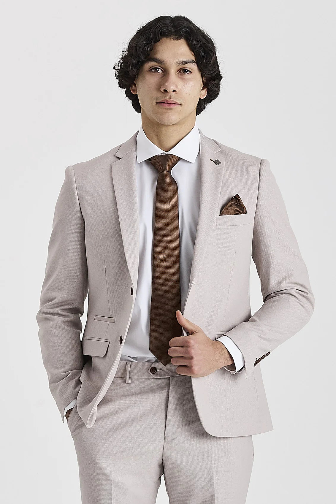 Close-up of a man wearing a stone beige three-piece suit with a white shirt and goldish brown paisley tie, adjusting his blazer.