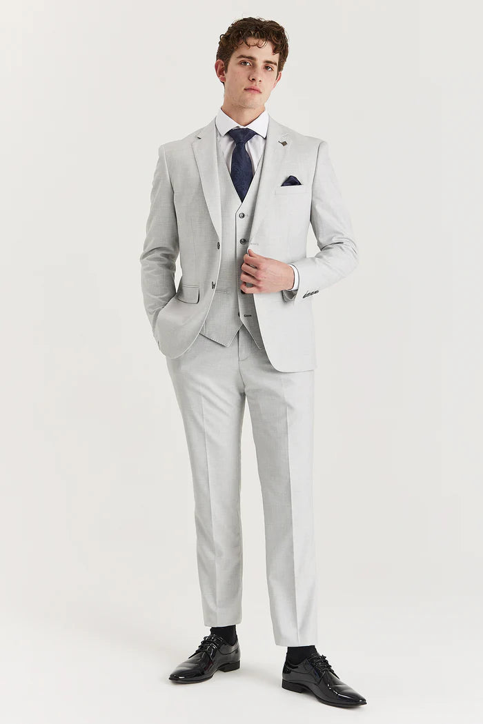Full view of a man wearing a tailored silver three-piece suit with black shoes, navy tie, and pocket square.