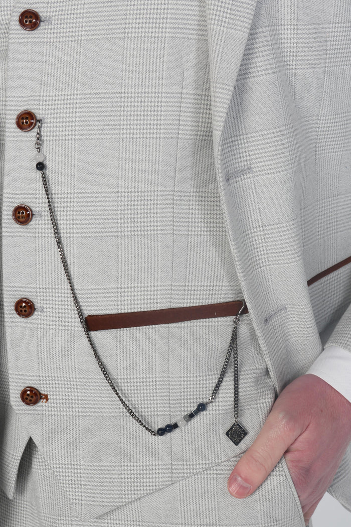 Close-up of the waistcoat pocket with a decorative chain accessory against the soft stone check pattern.