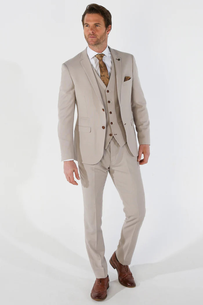 Full-length image of a man walking in a stone textured three-piece suit, paired with brown shoes and a patterned gold brown tie.
