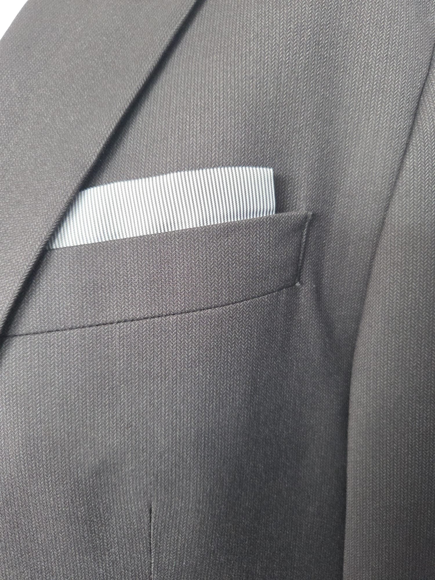 Herringbone fabric close-up on jacket chest pocket with folded pocket square.